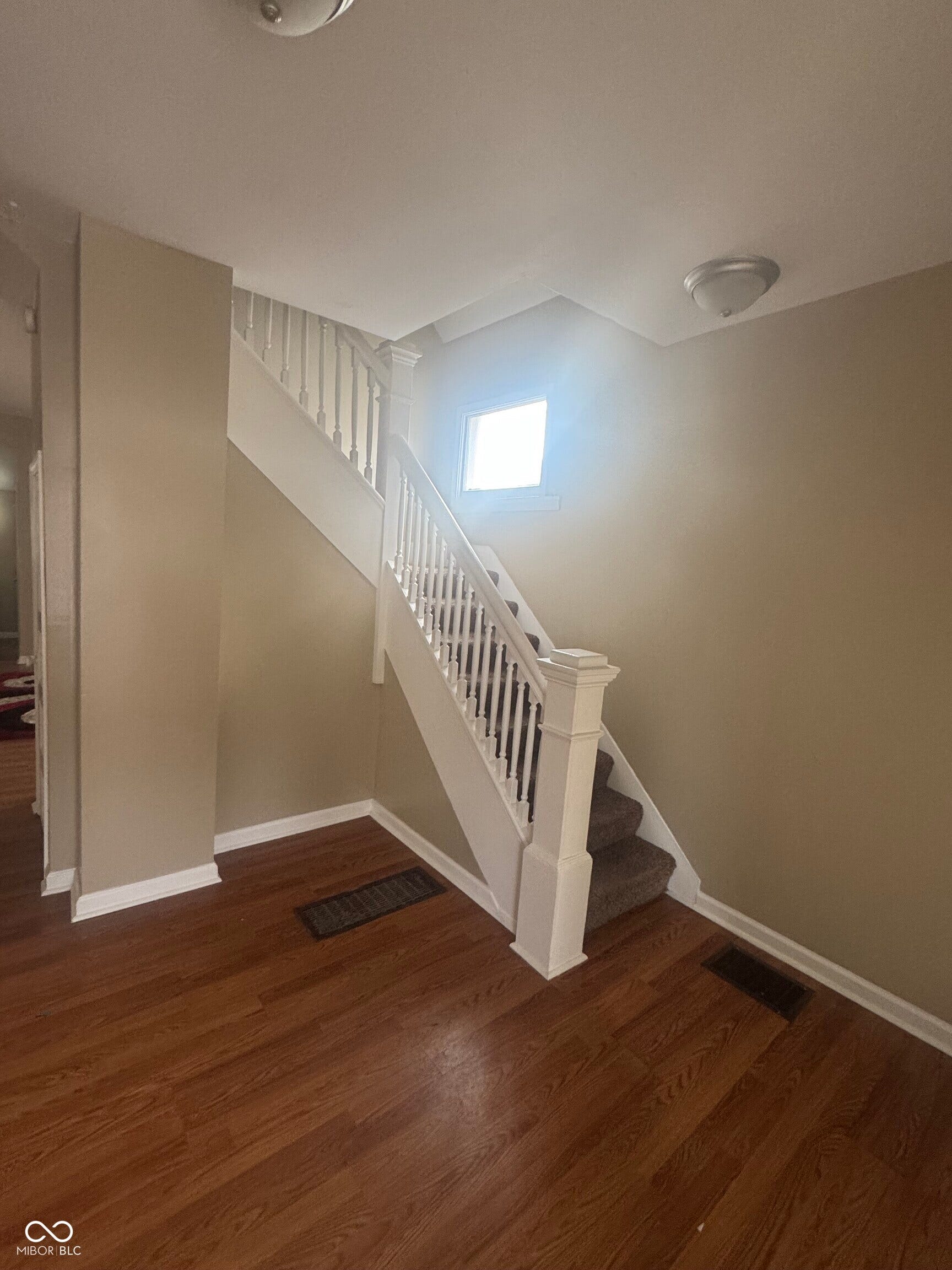 Virtually Altered - Wood-finish flooring, staircase with white newel post and balusters, carpeted treads, and natural light from a window