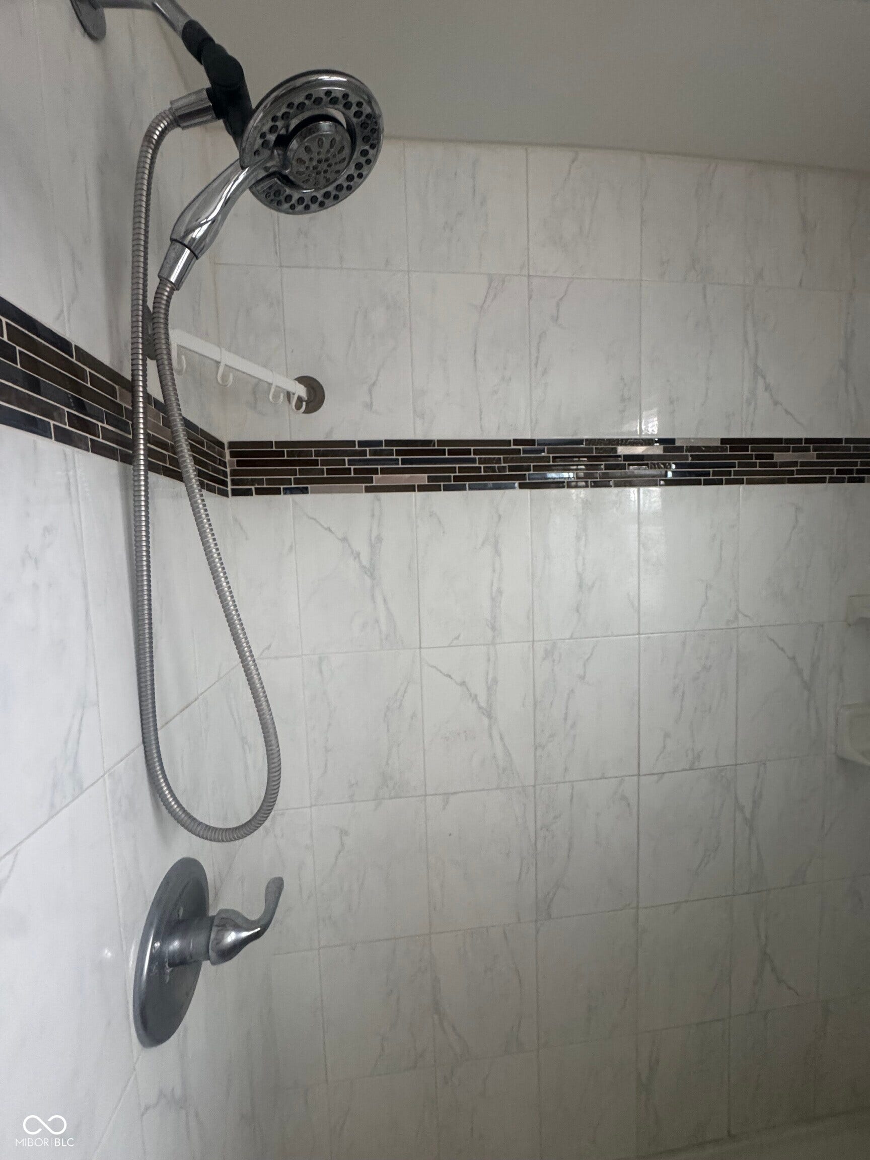 Virtually Altered - White tile shower with mosaic tile accent band, chrome shower fixture, and a handheld showerhead