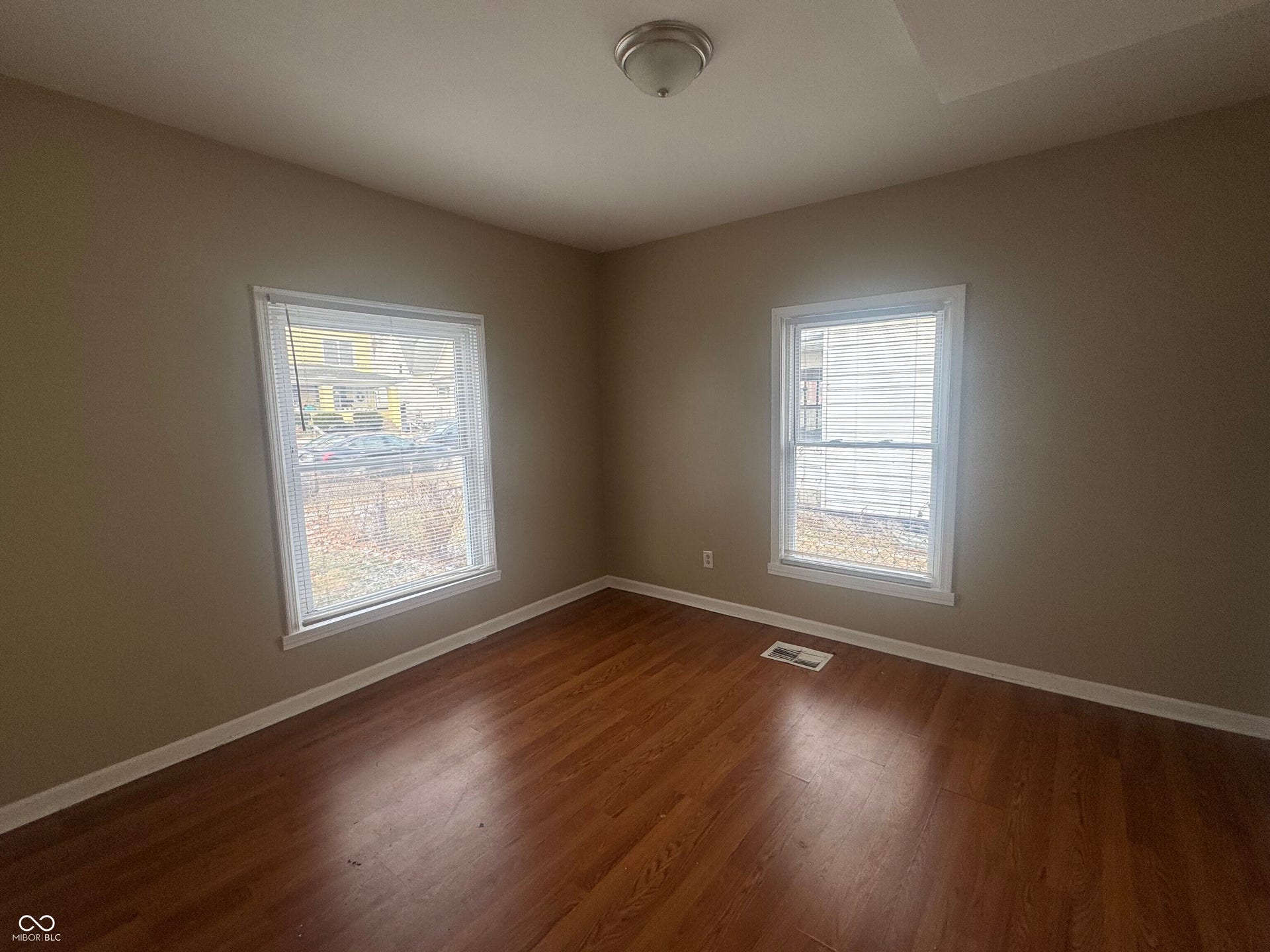 Virtually Altered - Wood-finish flooring with a neutral wall color, two windows with blinds, and a flush mount ceiling light fixture