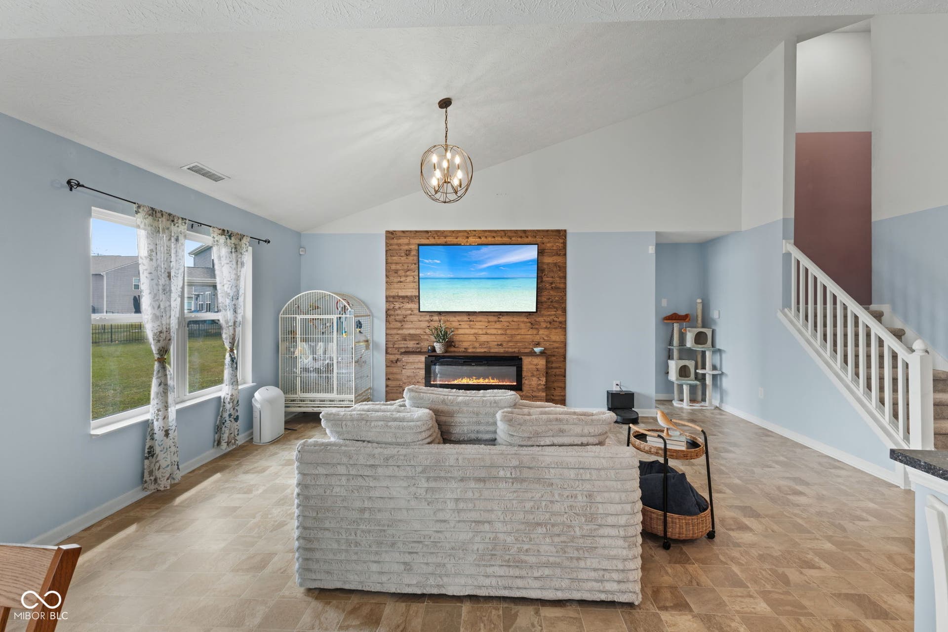 4643 Darla Court, Indianapolis, IN 46239 Vaulted ceiling, vinyl flooring, accent wall with electric fireplace, staircase with white railing, and multiple windows