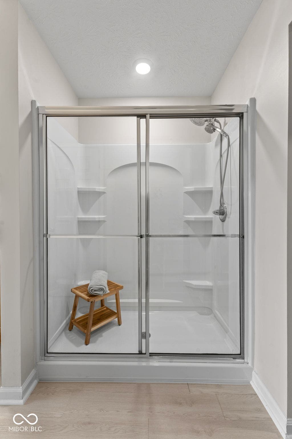 4643 Darla Court, Indianapolis, IN 46239 White shower enclosure with clear glass sliding doors, built-in shelving, and a handheld shower fixture