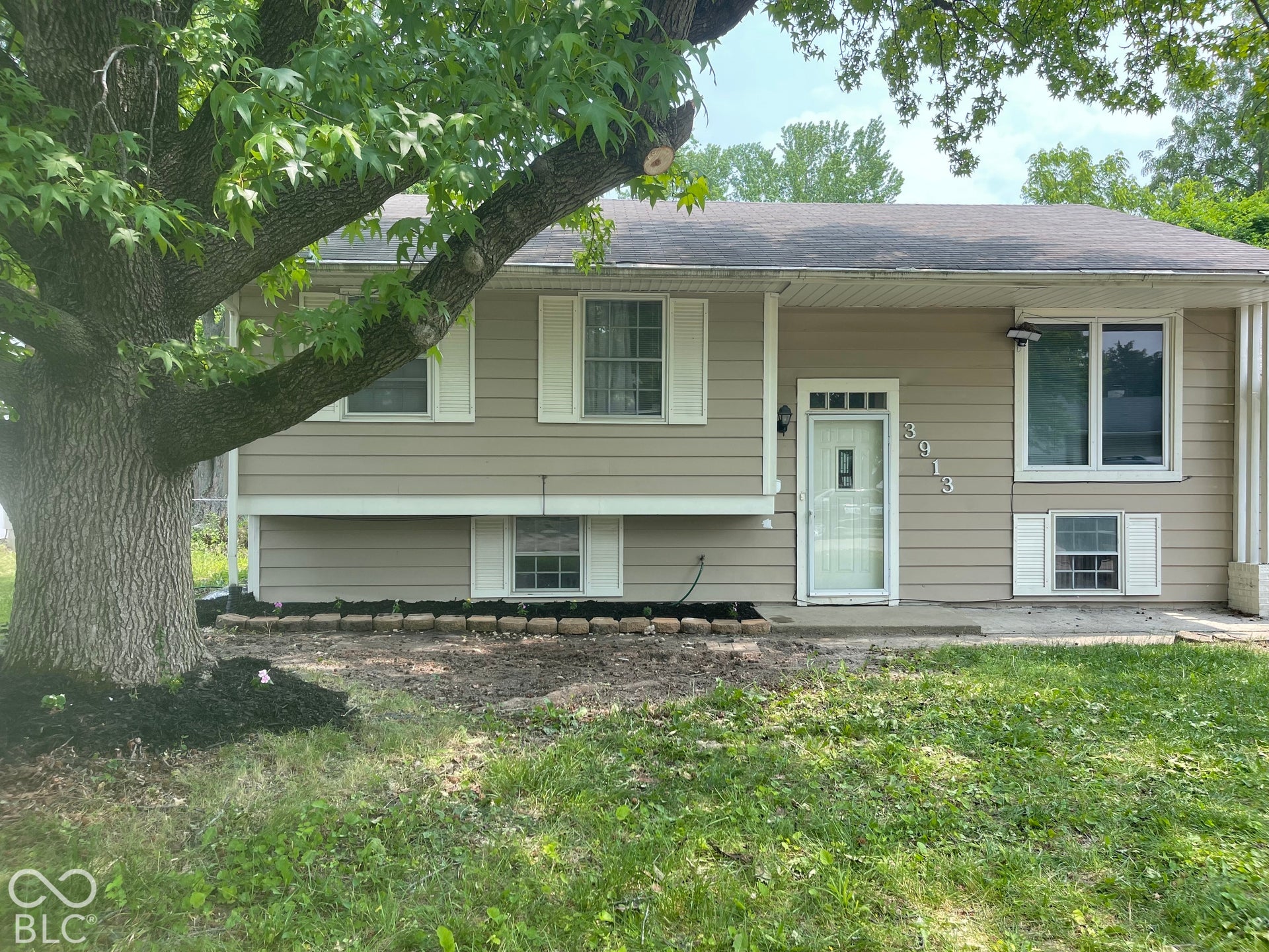 3913 Eisenhower Drive, Indianapolis, IN 46254 Split-level residence featuring beige siding, white window shutters, and a prominent mature tree