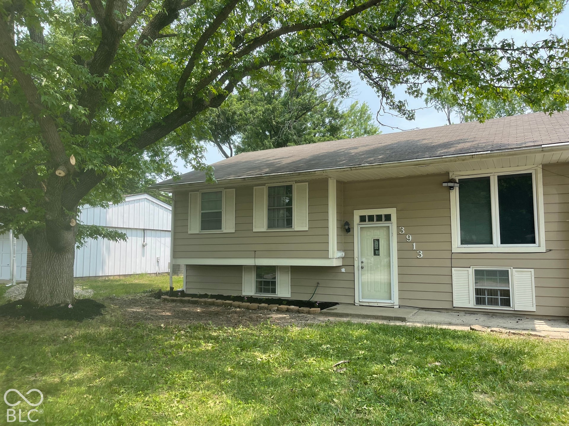 3913 Eisenhower Drive, Indianapolis, IN 46254 Split-level residence featuring tan siding, white window trim, and a prominent mature tree