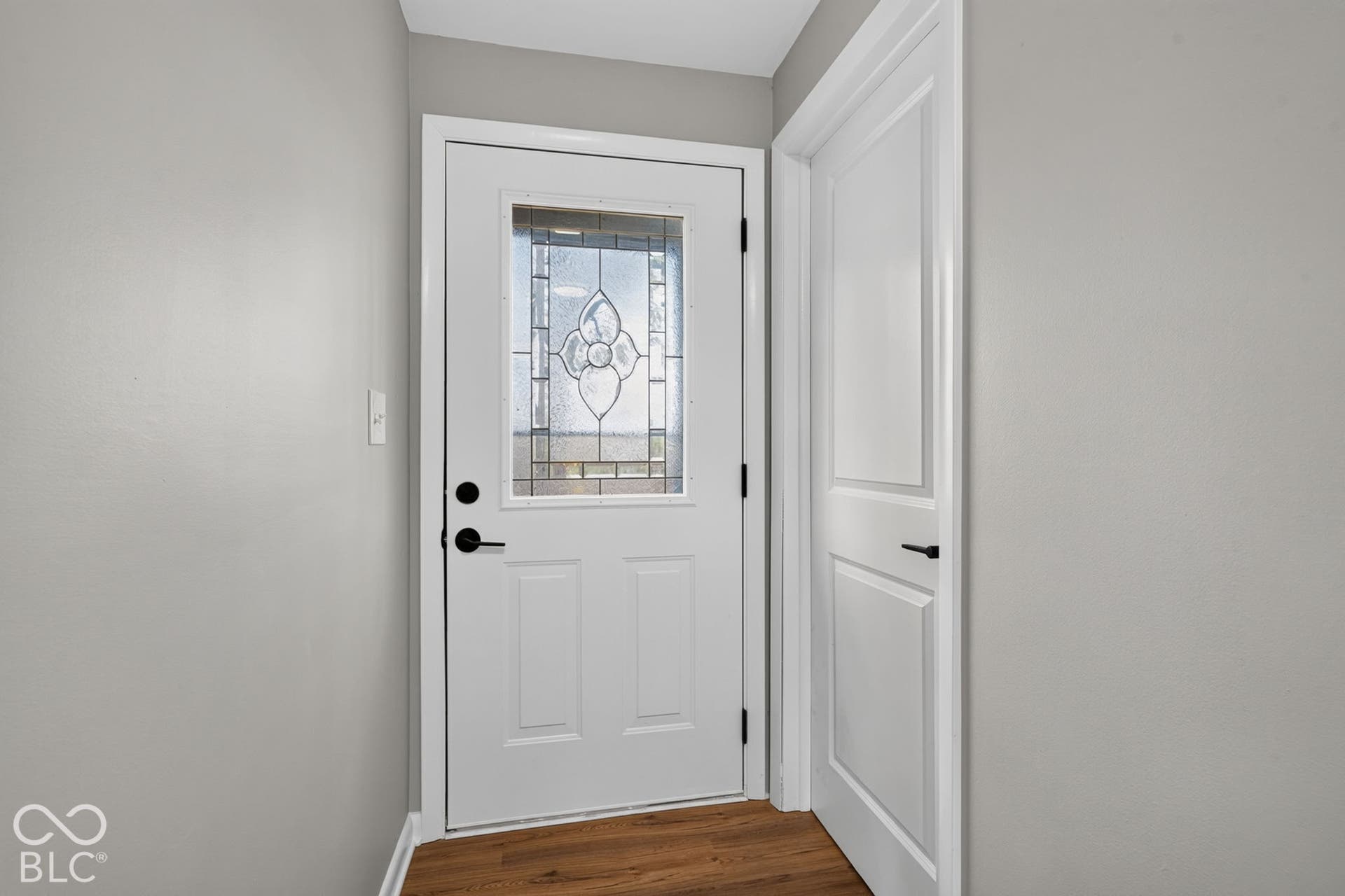 Entry door featuring a decorative glass insert, complemented by matte black hardware and wood-finish flooring