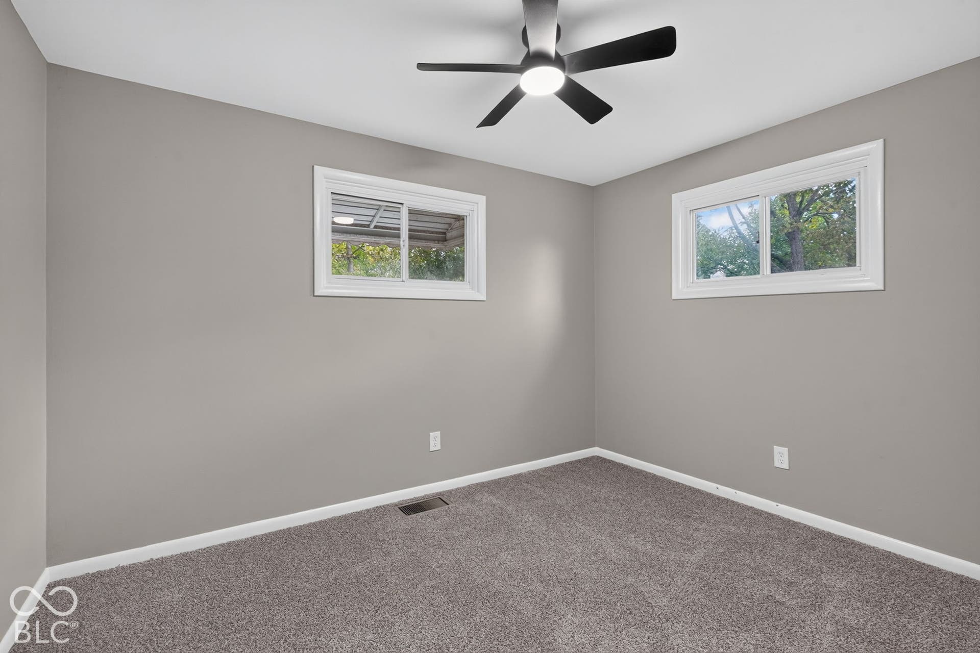 Neutral interior room with plush carpeting, dual sliding windows, and a matte black ceiling fan with integrated lighting