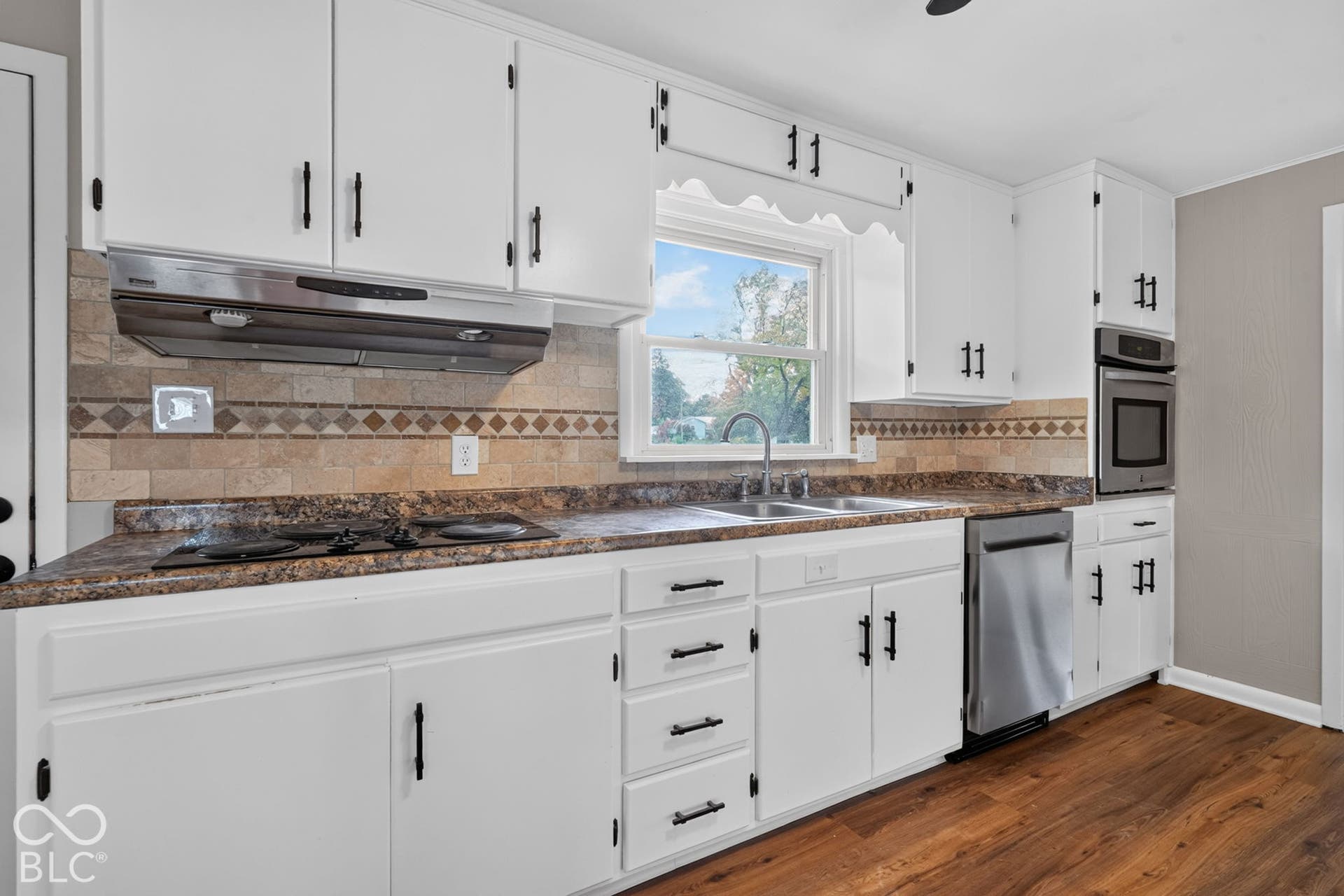 Kitchen featuring white cabinetry with matte black hardware, stone-tile backsplash, laminate countertops, wood-finish flooring, and stainless steel appliances