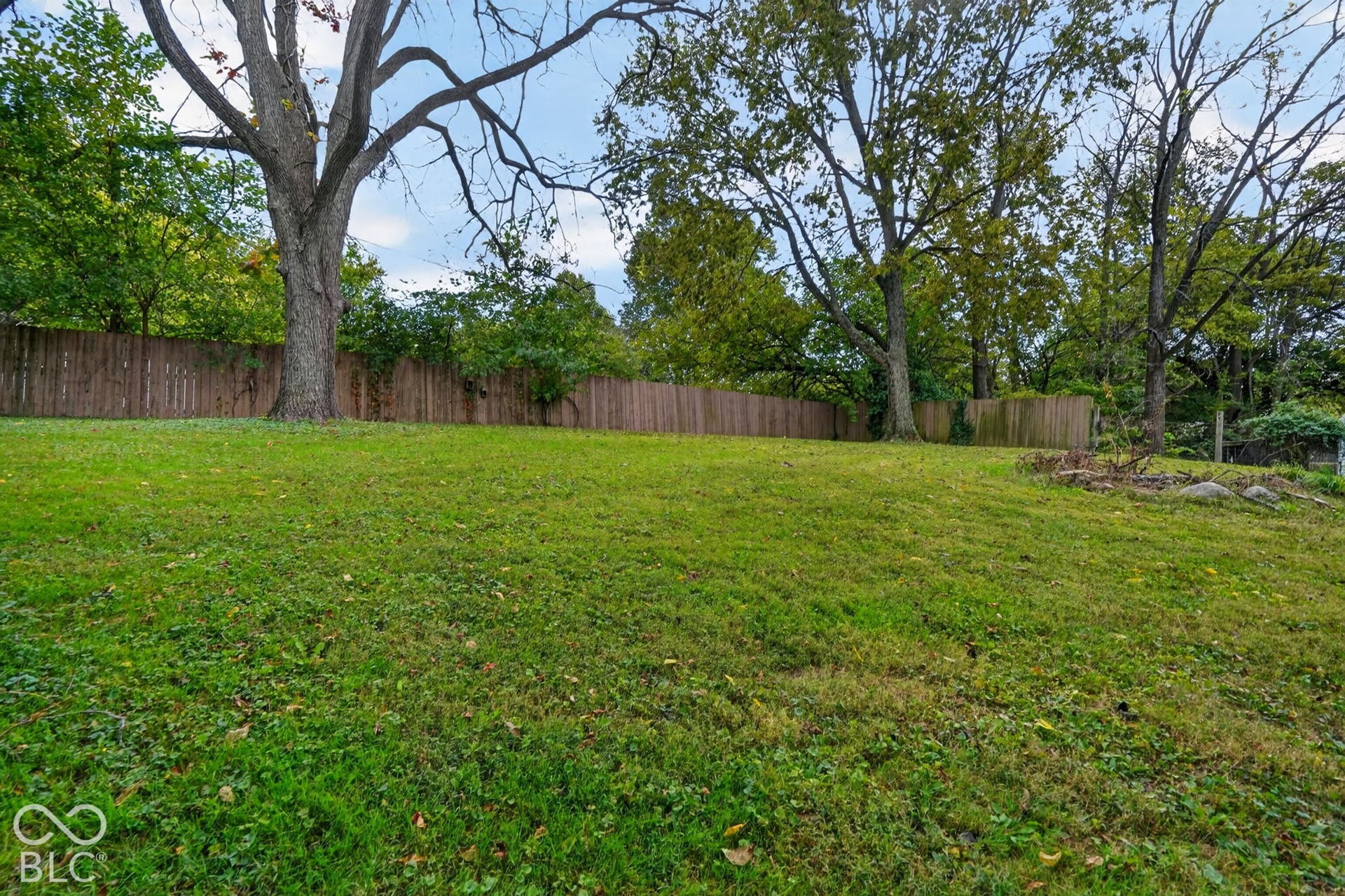 Expansive backyard featuring a lawn, mature trees, and a wooden perimeter fence