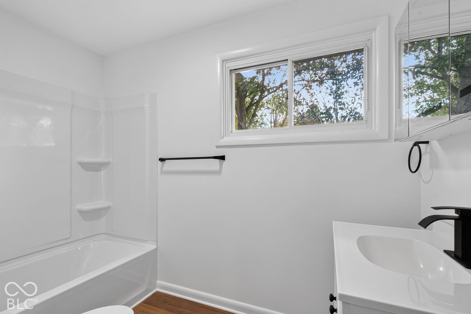 Bathroom featuring a white tub-shower combination, a vanity with a white countertop, a black faucet, a sliding window, and wood-finish flooring