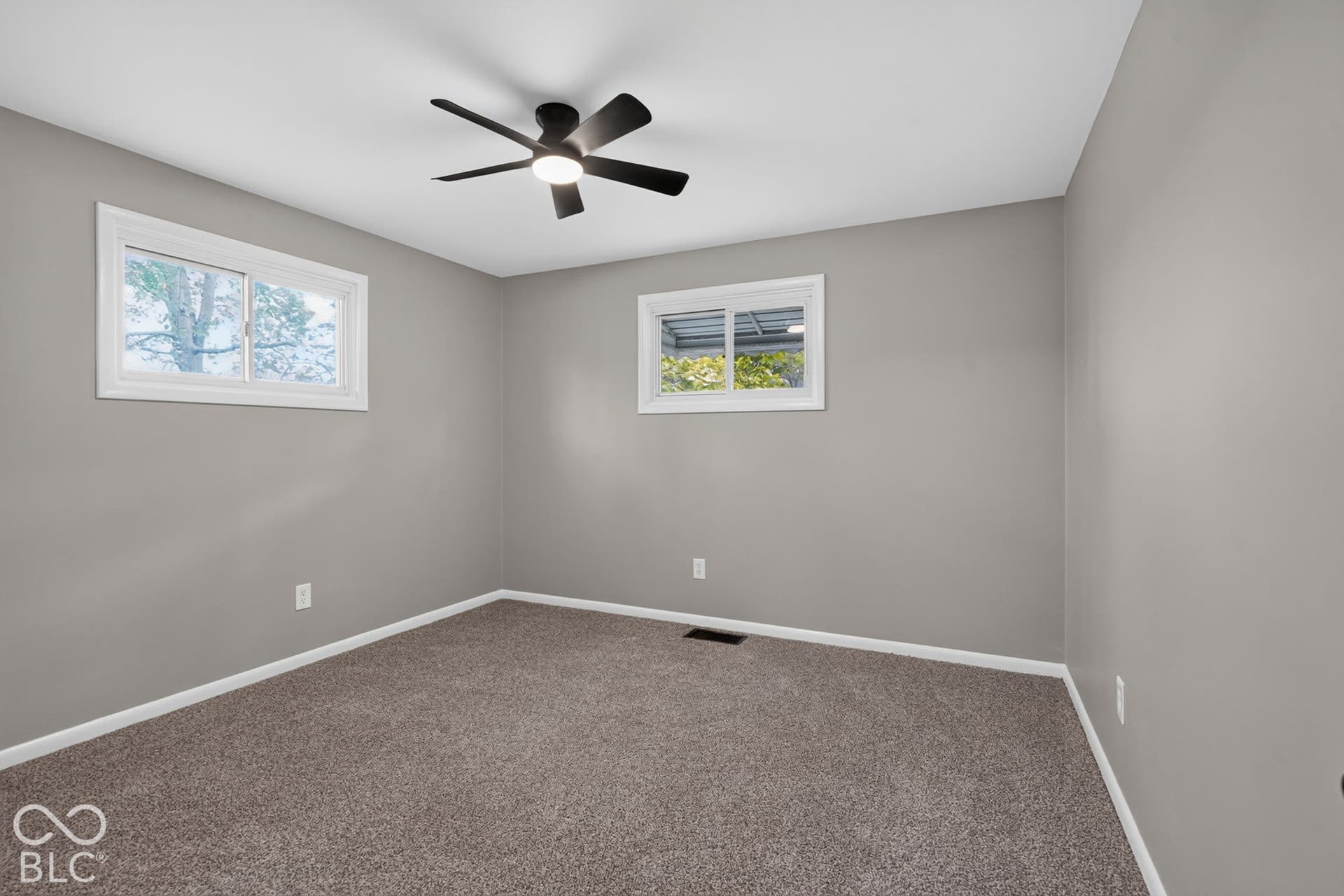 Neutral-toned interior space featuring wall-to-wall carpeting, two sliding windows, and a ceiling fan with integrated lighting