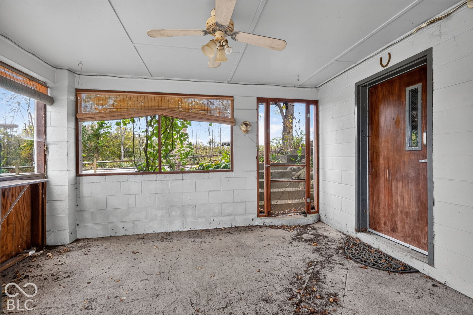 Enclosed porch featuring concrete flooring, painted masonry walls, a ceiling-mounted fan with integrated lighting, and a wood-finish entry door with a vertical glass insert
