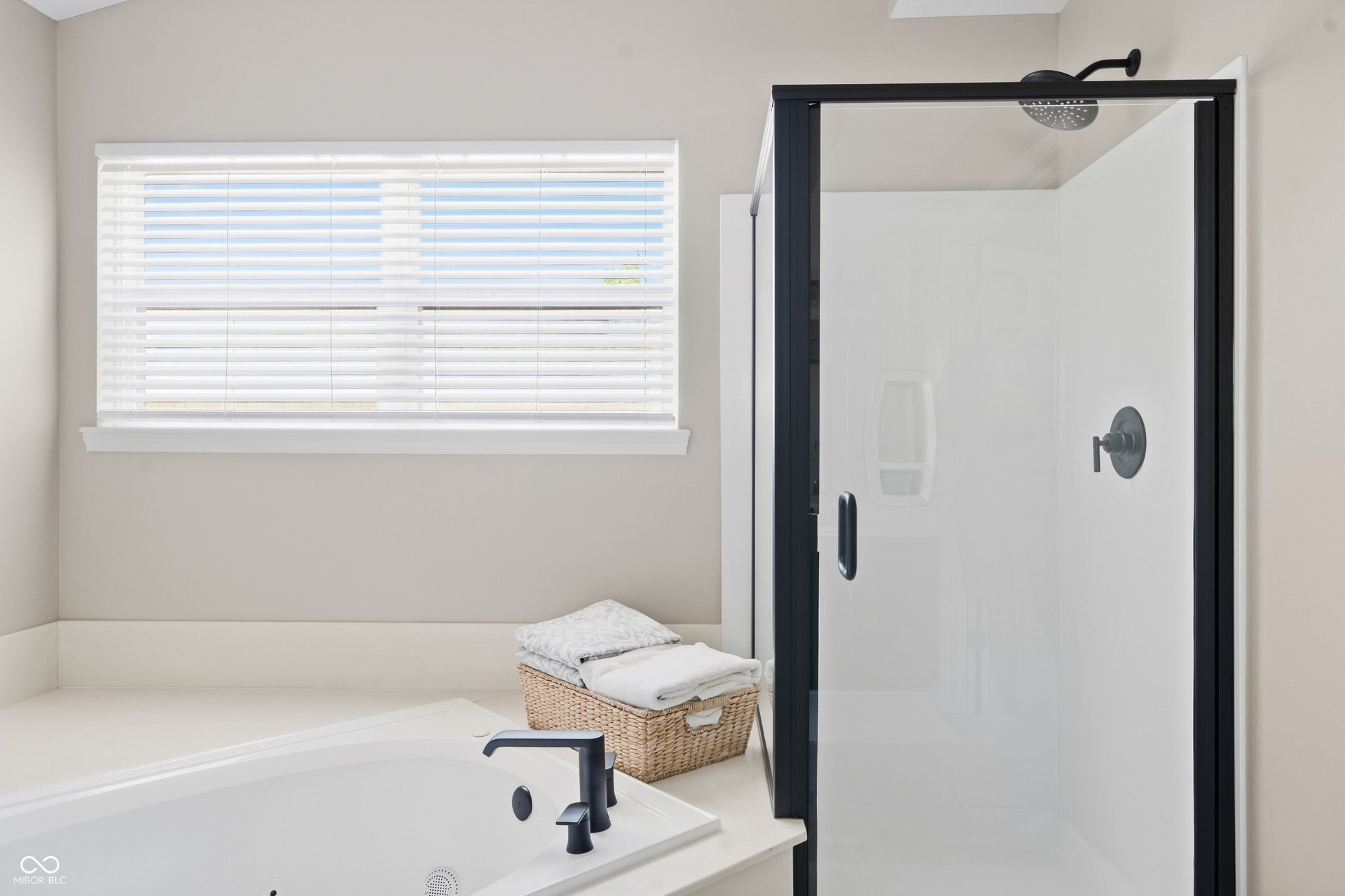 Soaking tub with matte black fixtures, white window blinds, and a separate walk-in shower with black-framed glass enclosure