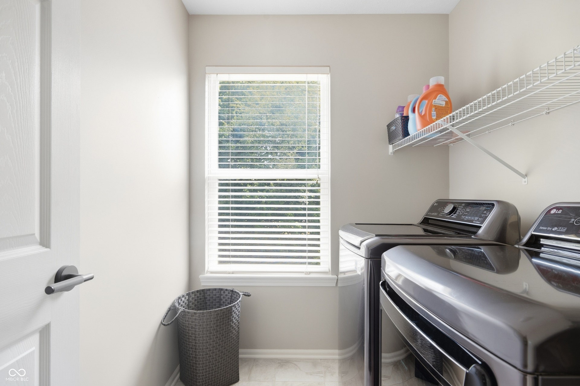 Laundry area with tile flooring, a window featuring blinds, and a permanent wire shelf for storage