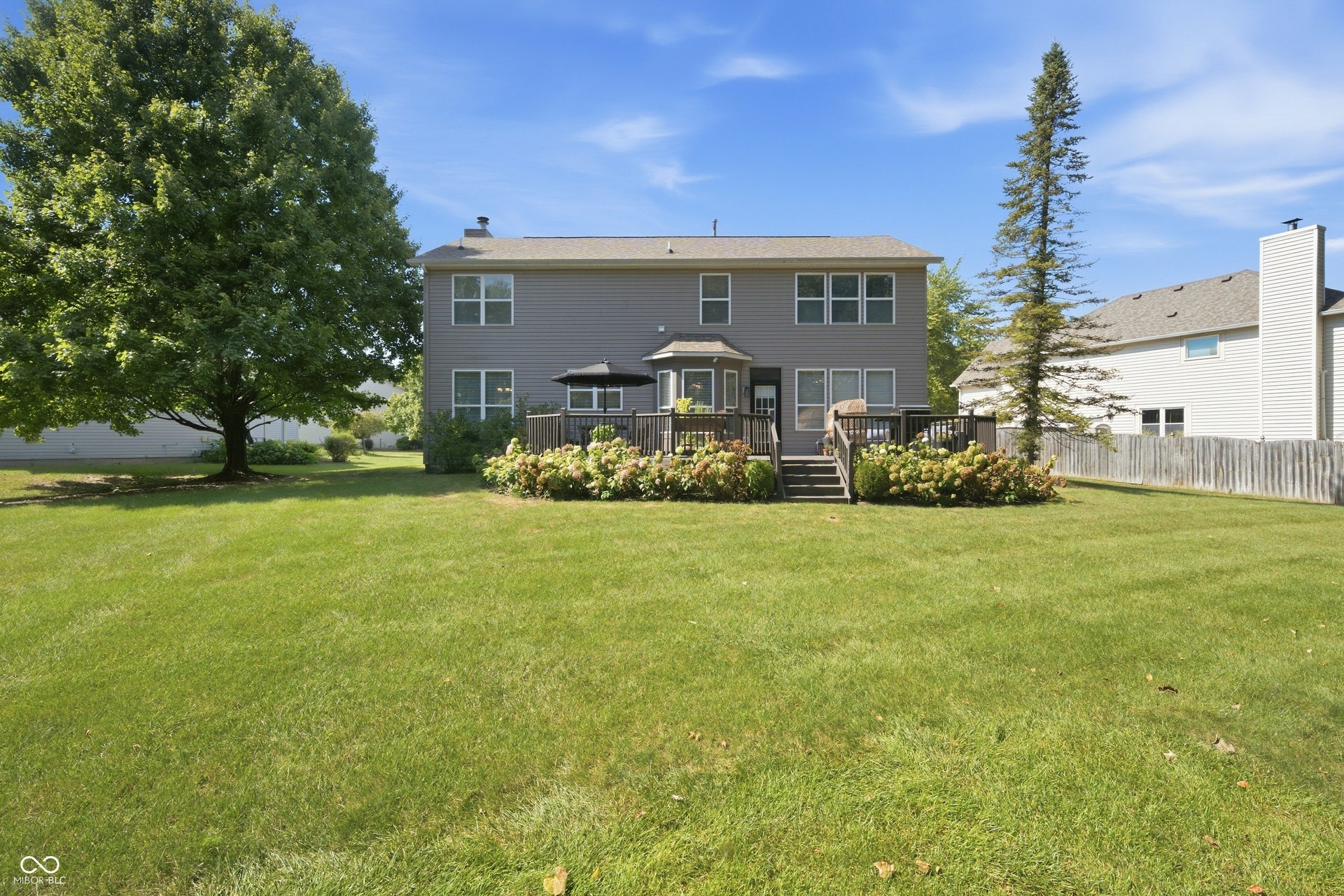 Expansive backyard with a manicured lawn, established mature trees, multi-level wood deck, and perimeter landscaping