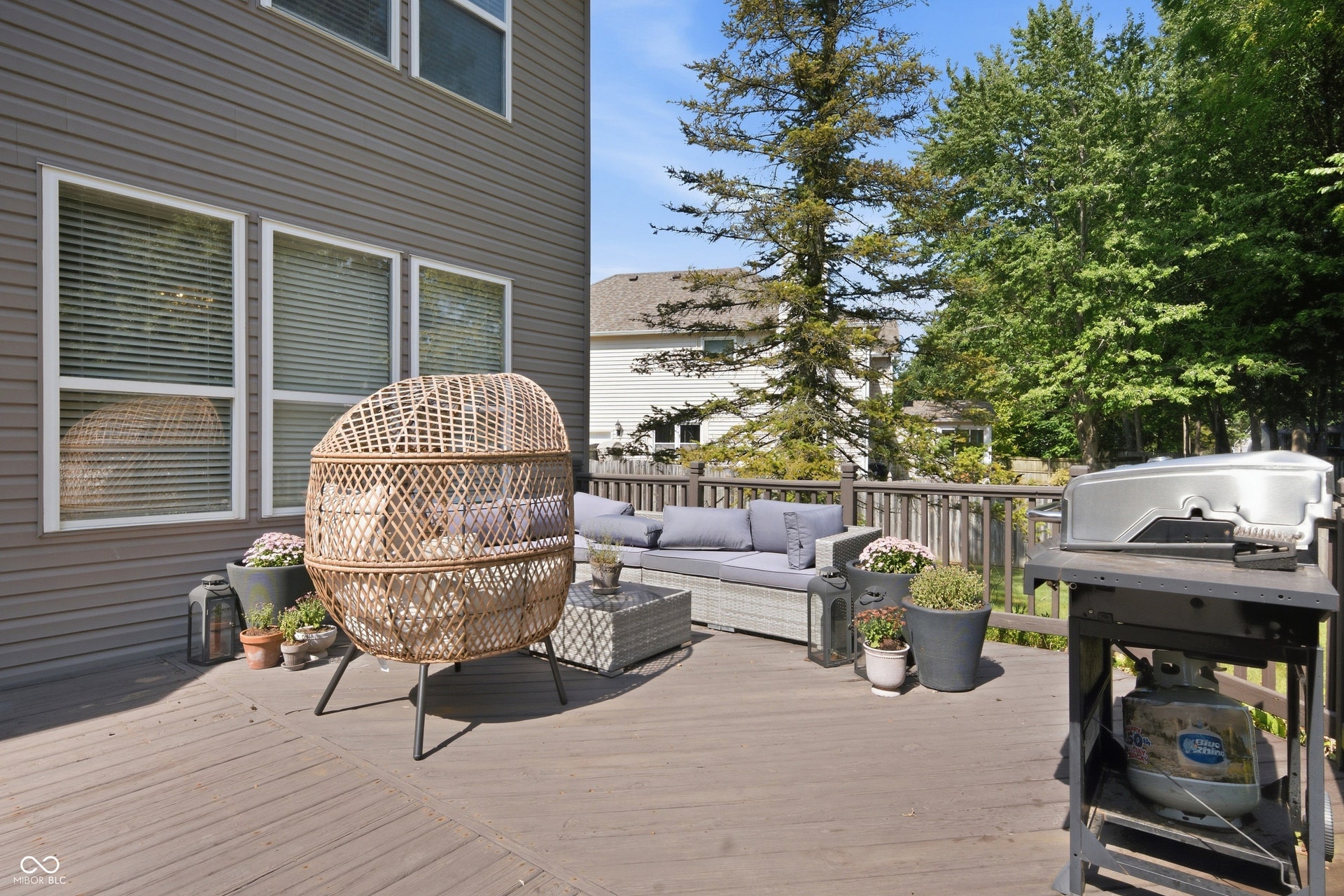 Expansive outdoor deck with wood-finish flooring, surrounded by mature trees, and featuring horizontal siding
