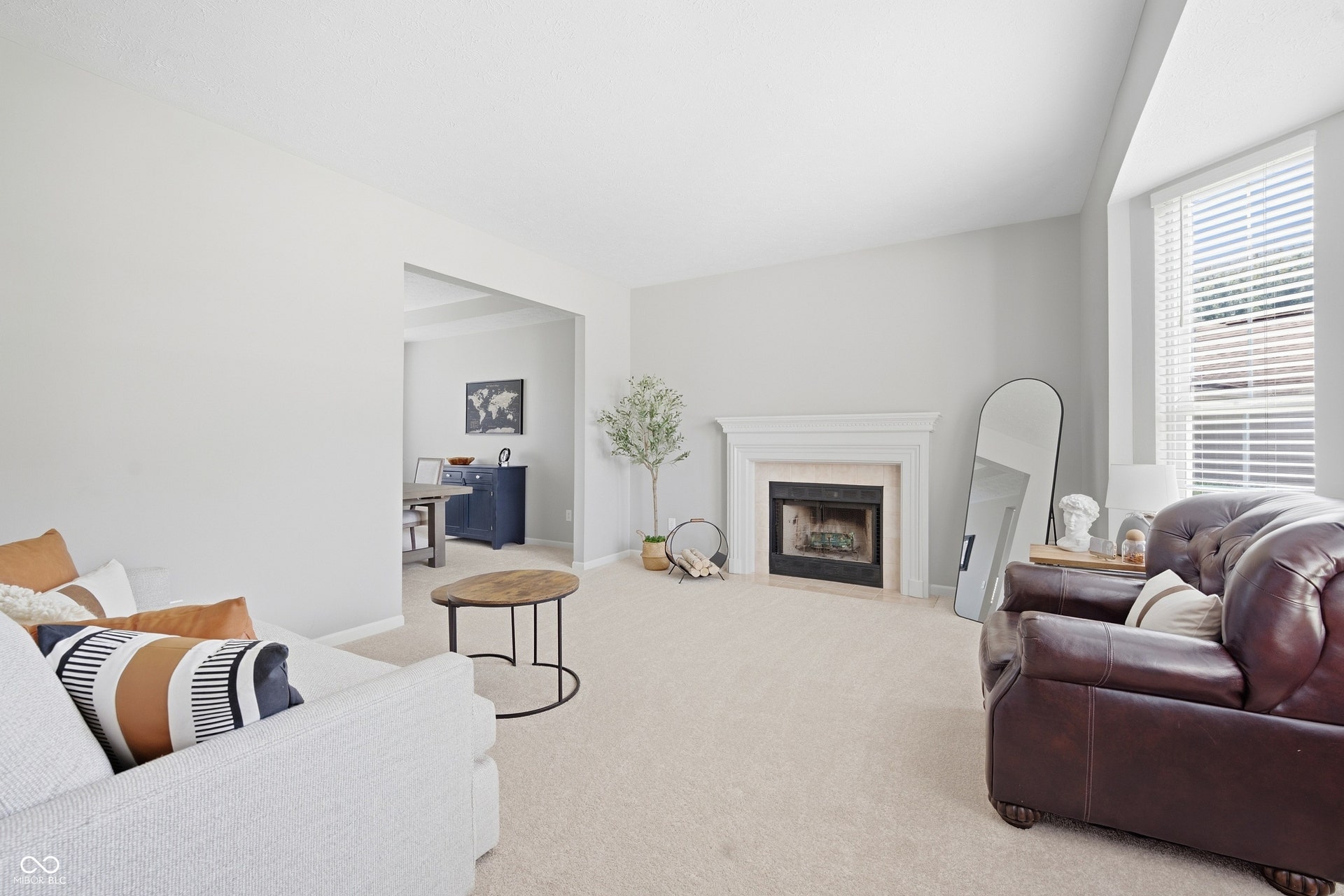 Recessed fireplace with a white mantel, light-toned carpeting, and a bay window