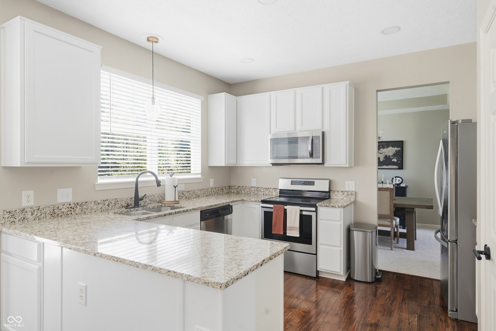 U-shaped kitchen with white cabinetry, light-toned countertops, and wood-finish flooring