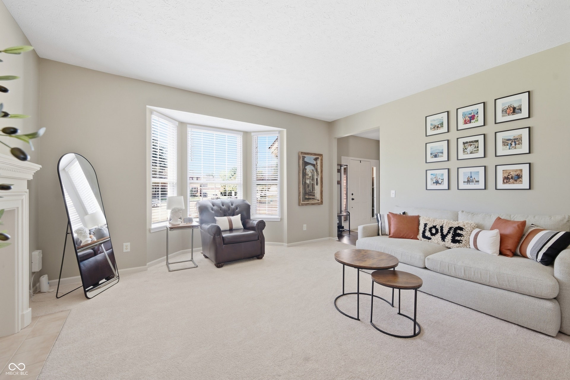 Recessed bay window with blinds, light-toned carpeting, and a white fireplace mantel