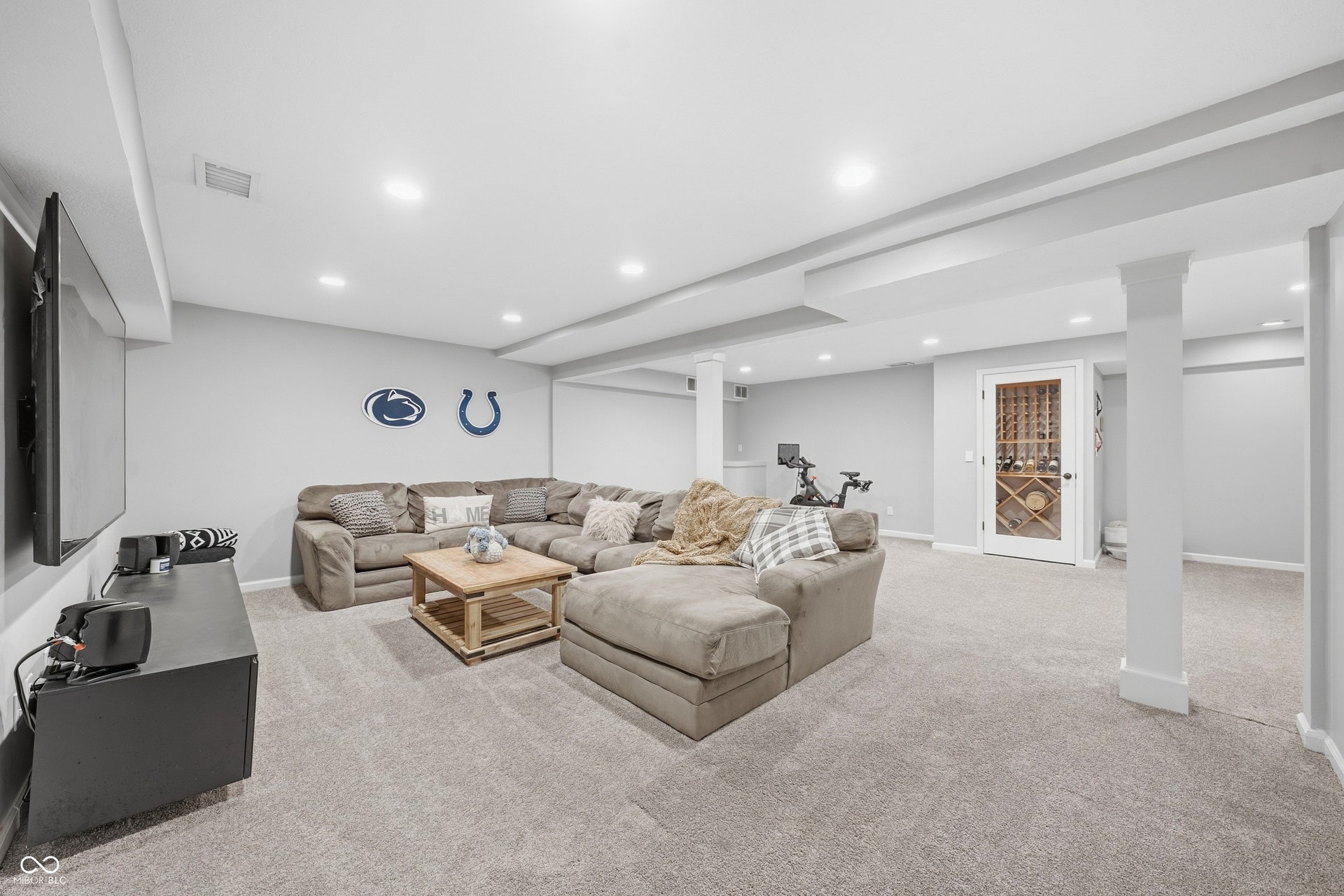 Recessed lighting, light gray carpeting, and a built-in wine storage room with a glass-paneled door