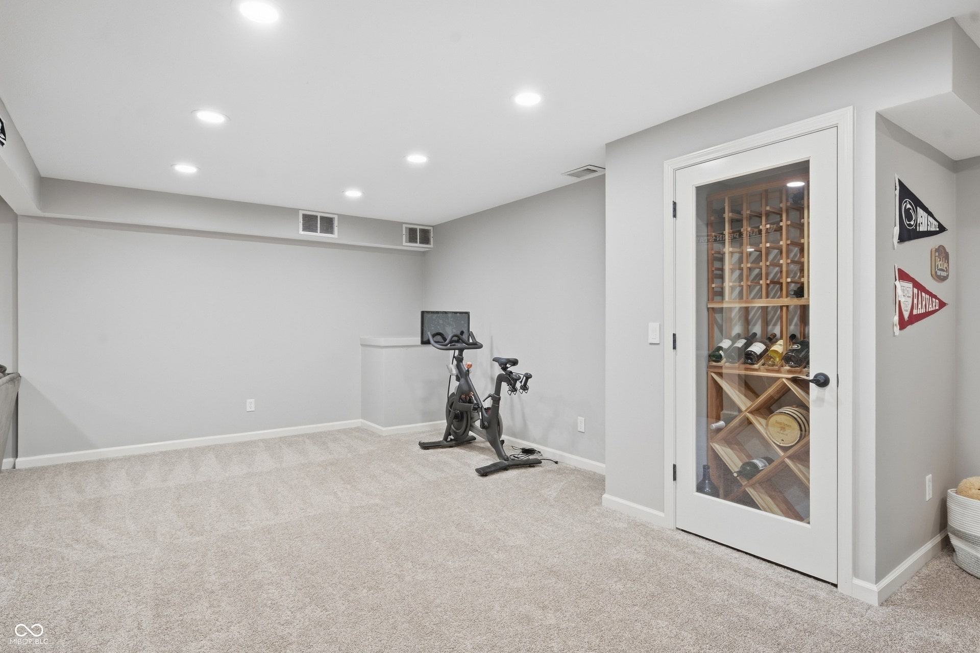 Recessed ceiling lighting, light gray wall paint, light-toned carpeting, and a built-in wine storage unit with a glass-paneled door