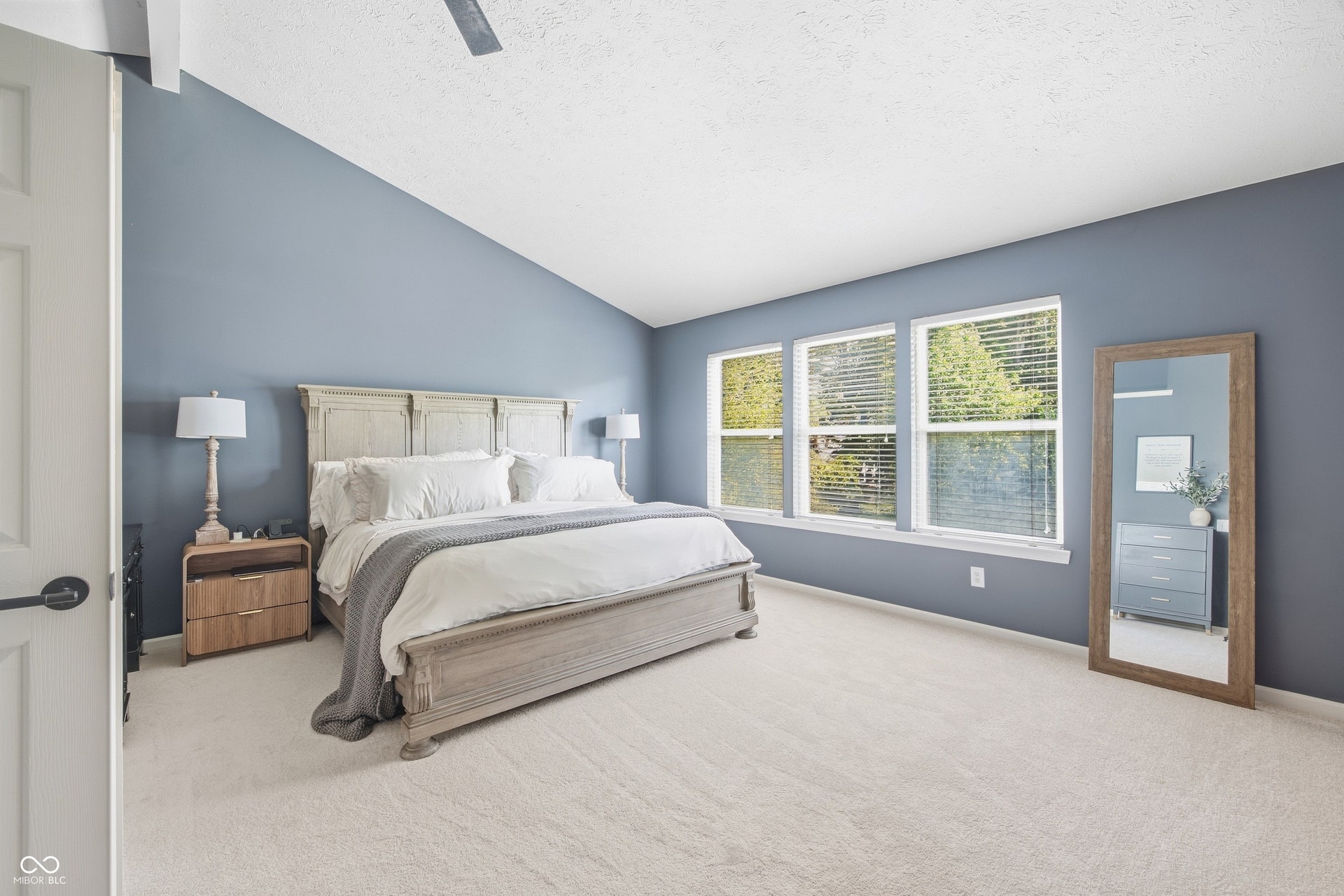 Vaulted ceiling with a ceiling fan, three paneled windows, and light-colored carpet flooring