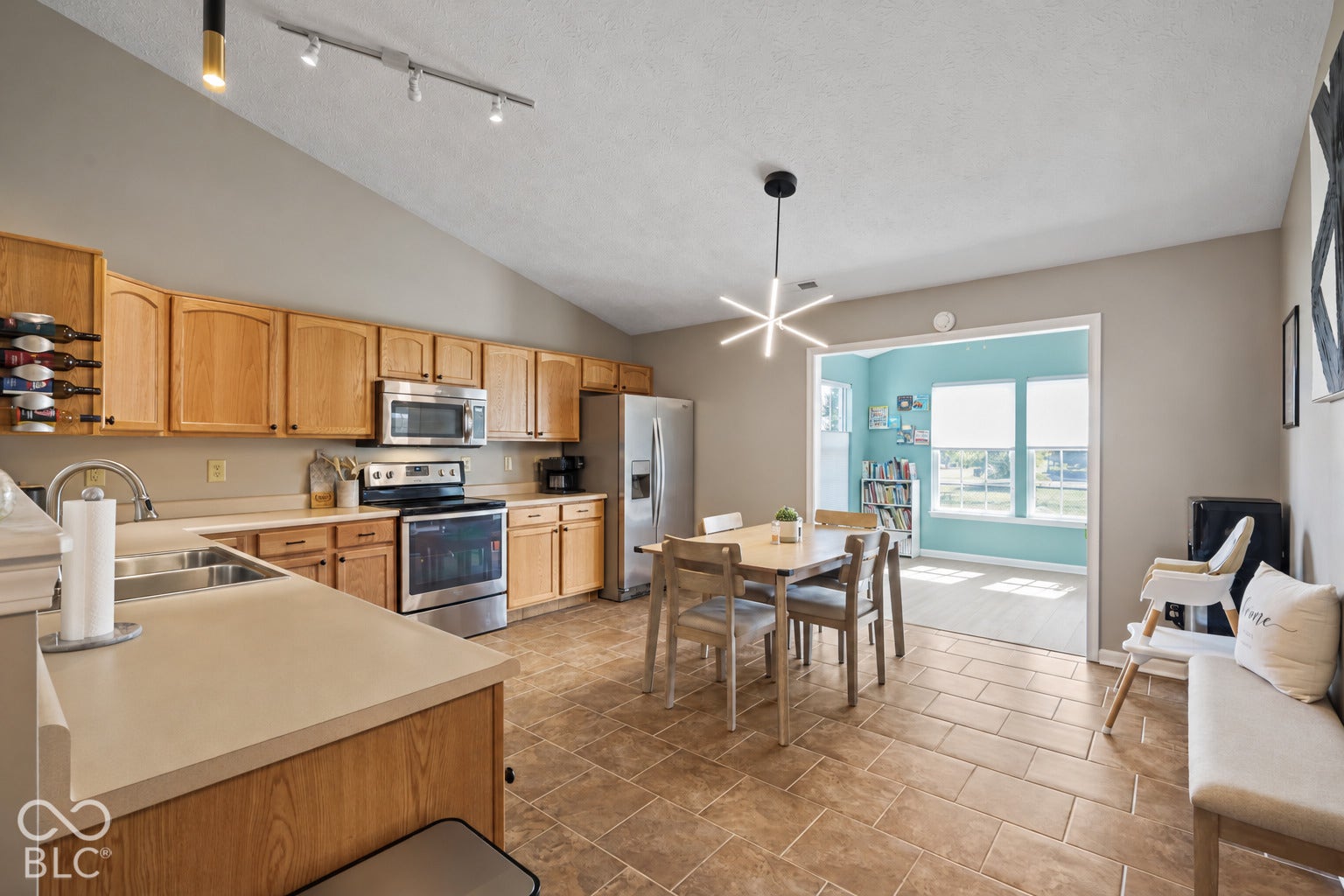 Open-concept kitchen and dining area featuring wood-finish cabinetry, stainless steel appliances, tile flooring, and expansive windows with sliding glass doors opening to a balcony with skyline views