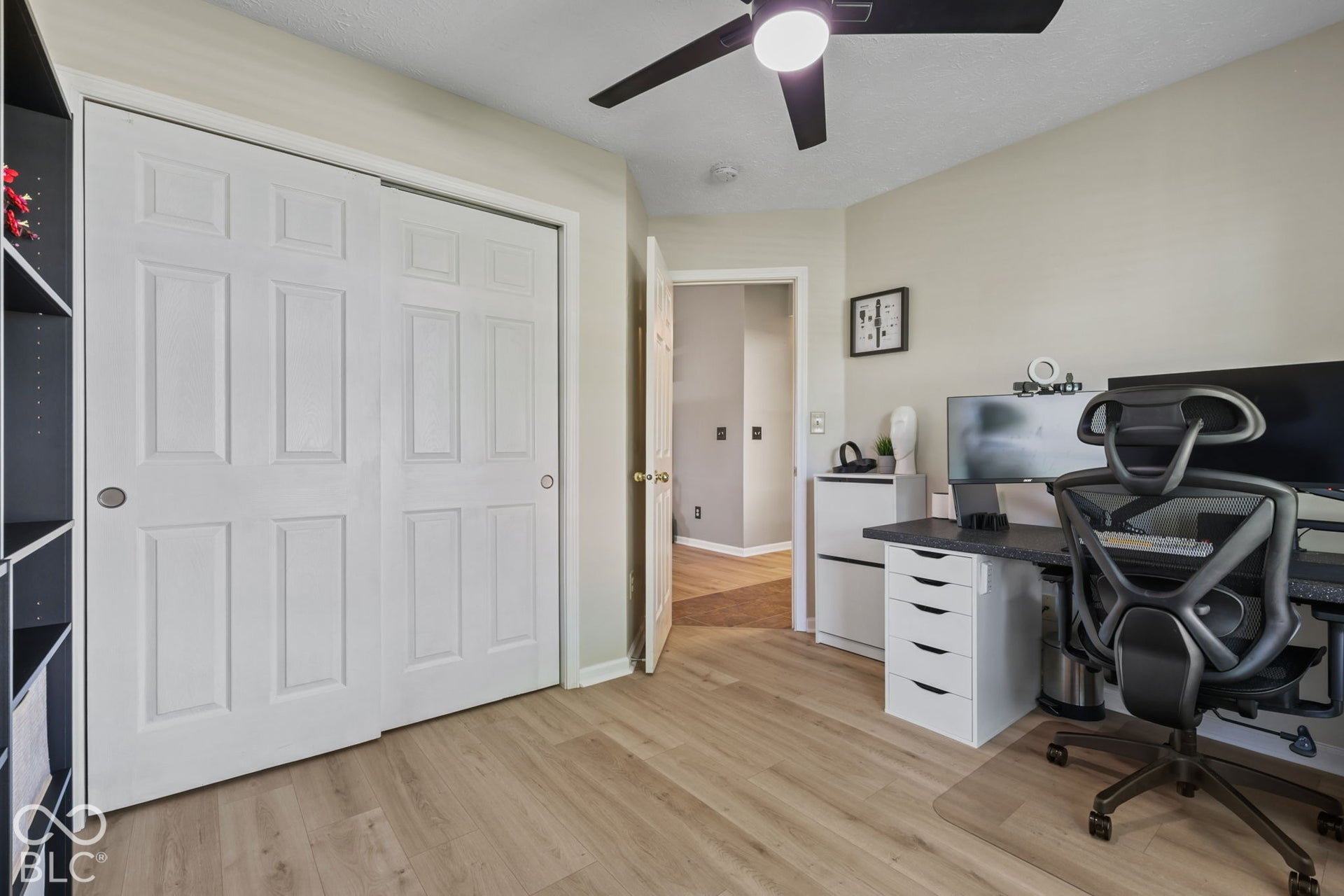 Dedicated home office featuring wood-finish flooring, a ceiling fan with integrated lighting, white panel closet doors, and built-in desk cabinetry with ample storage drawers