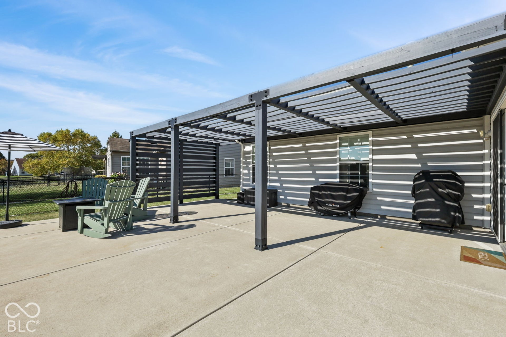 Concrete patio featuring a dark-toned metal pergola, slatted privacy screening, and light-colored siding