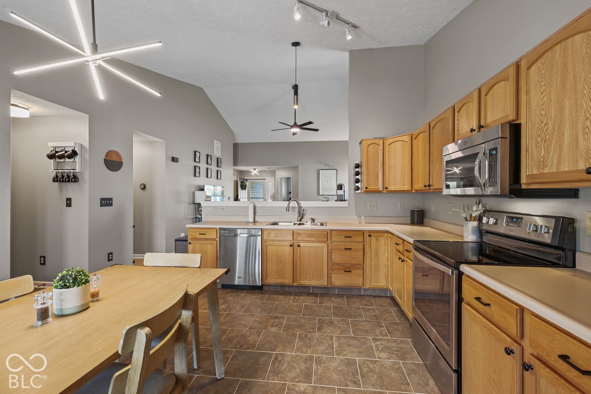 Kitchen featuring vaulted ceilings, wood cabinetry, stainless steel appliances, tile flooring, and contemporary overhead lighting