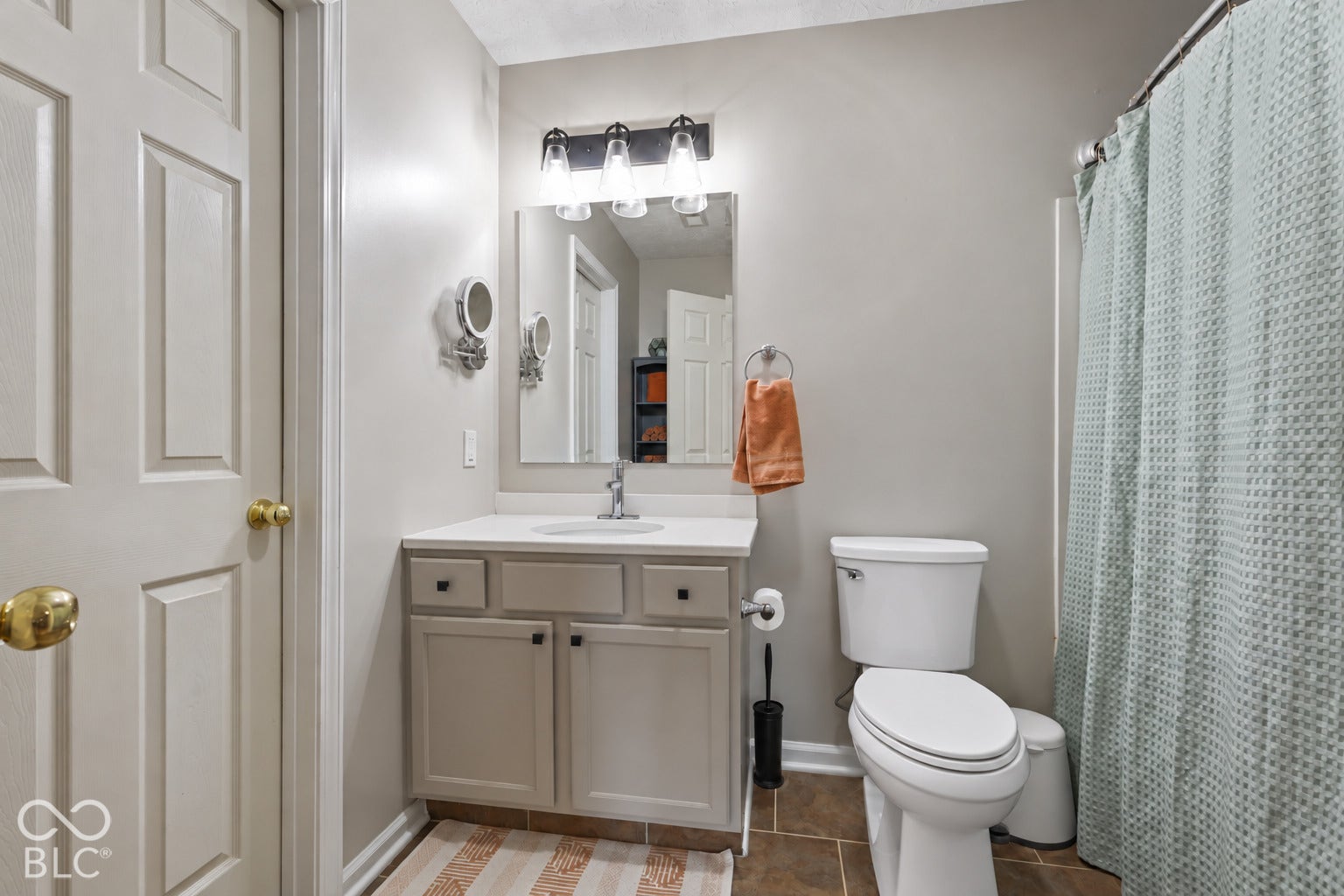 Neutral-toned vanity with a solid surface countertop, rectangular mirror, three-light fixture, and stone-finish flooring