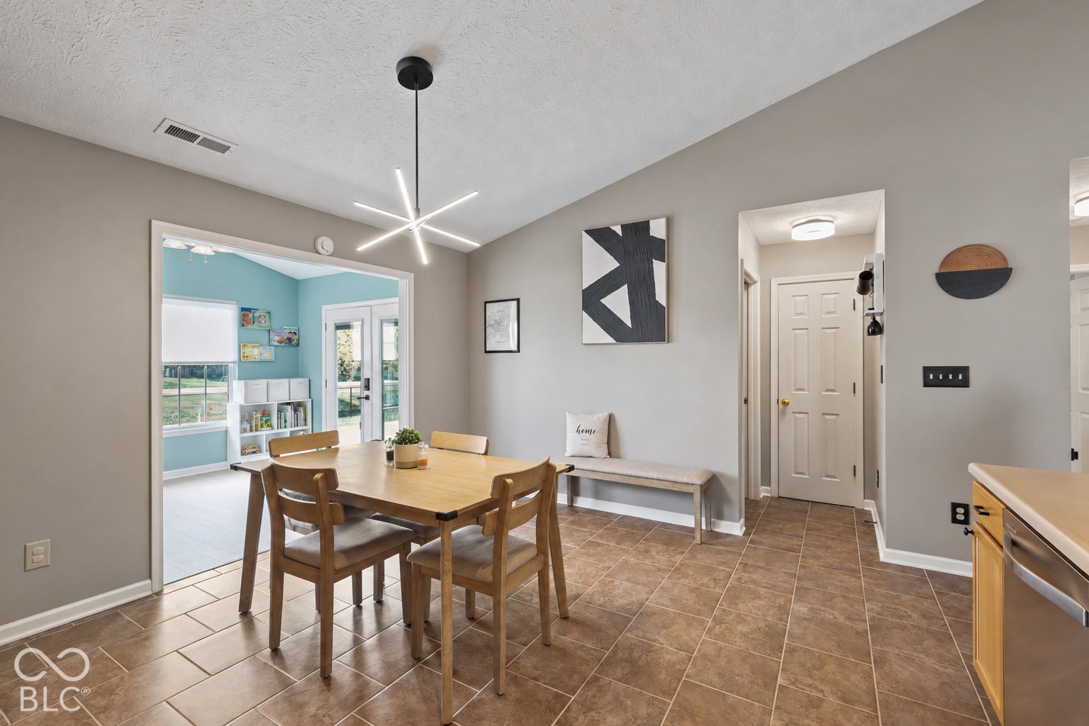 Vaulted ceiling with modern geometric chandelier, ceramic tile flooring, and six-panel interior door