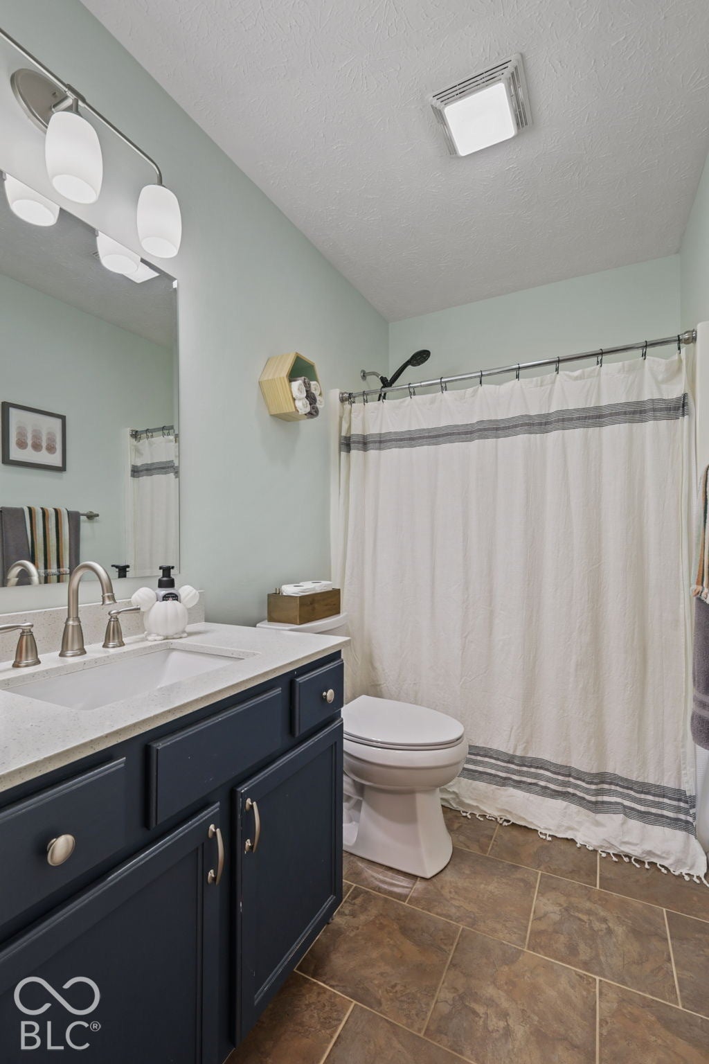 Bathroom vanity featuring navy cabinetry, stone-finish countertop, undermount sink, brushed nickel hardware, and tile flooring