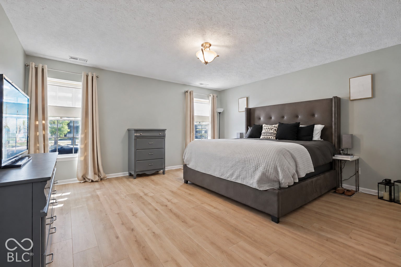 Neutral wall tones, wood-finish flooring, and multiple windows providing natural light, finished with a central ceiling-mounted light fixture