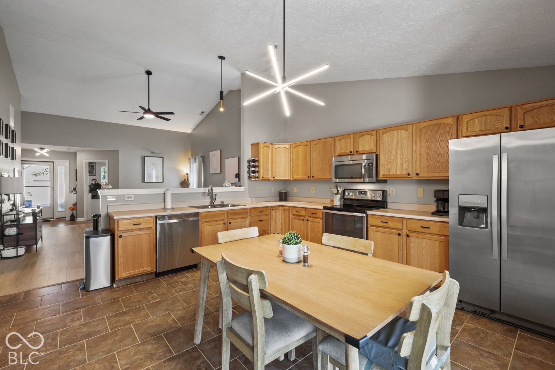 Kitchen featuring vaulted ceilings, wood cabinetry, stainless steel appliances, a geometric statement light fixture, and tile flooring