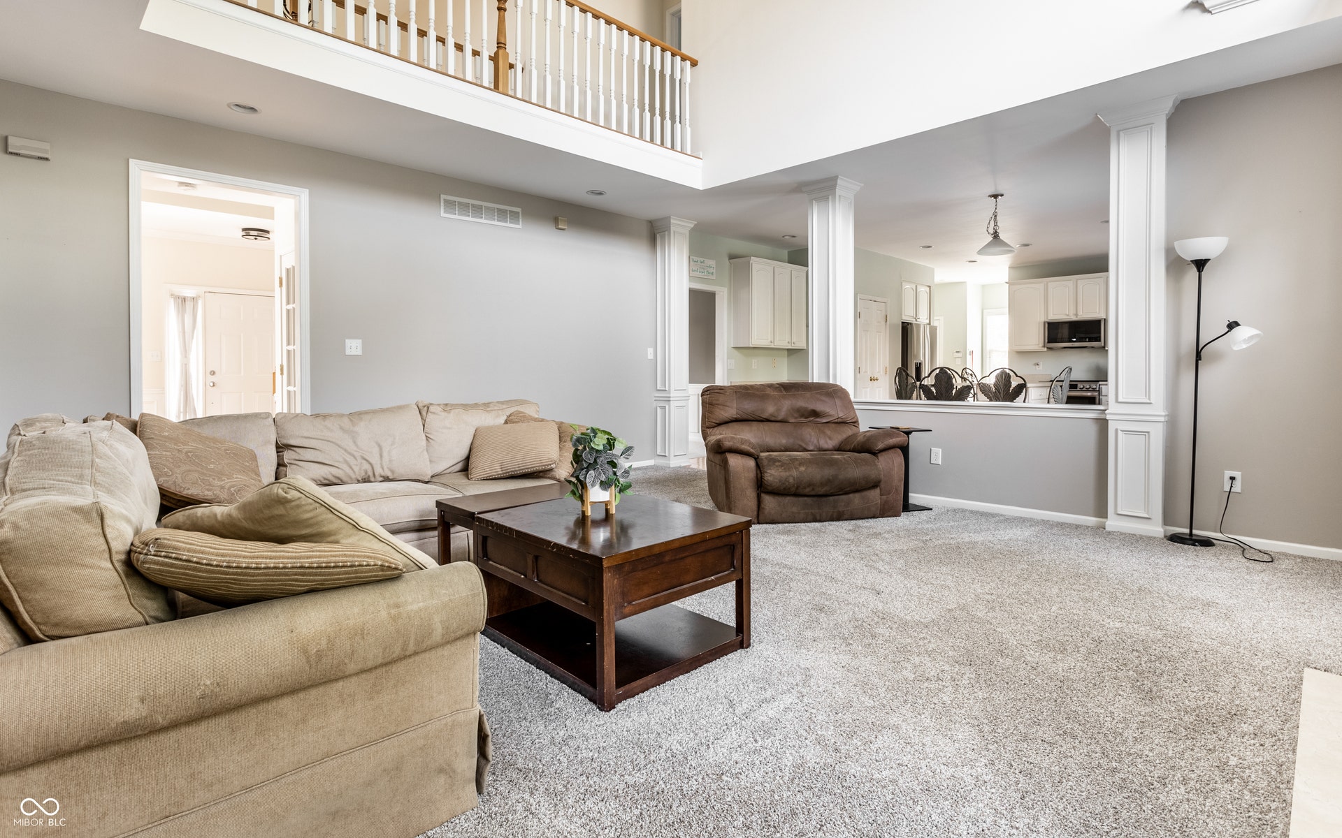 Two-story living area featuring decorative columns, and an upper-level railing overlooking the space