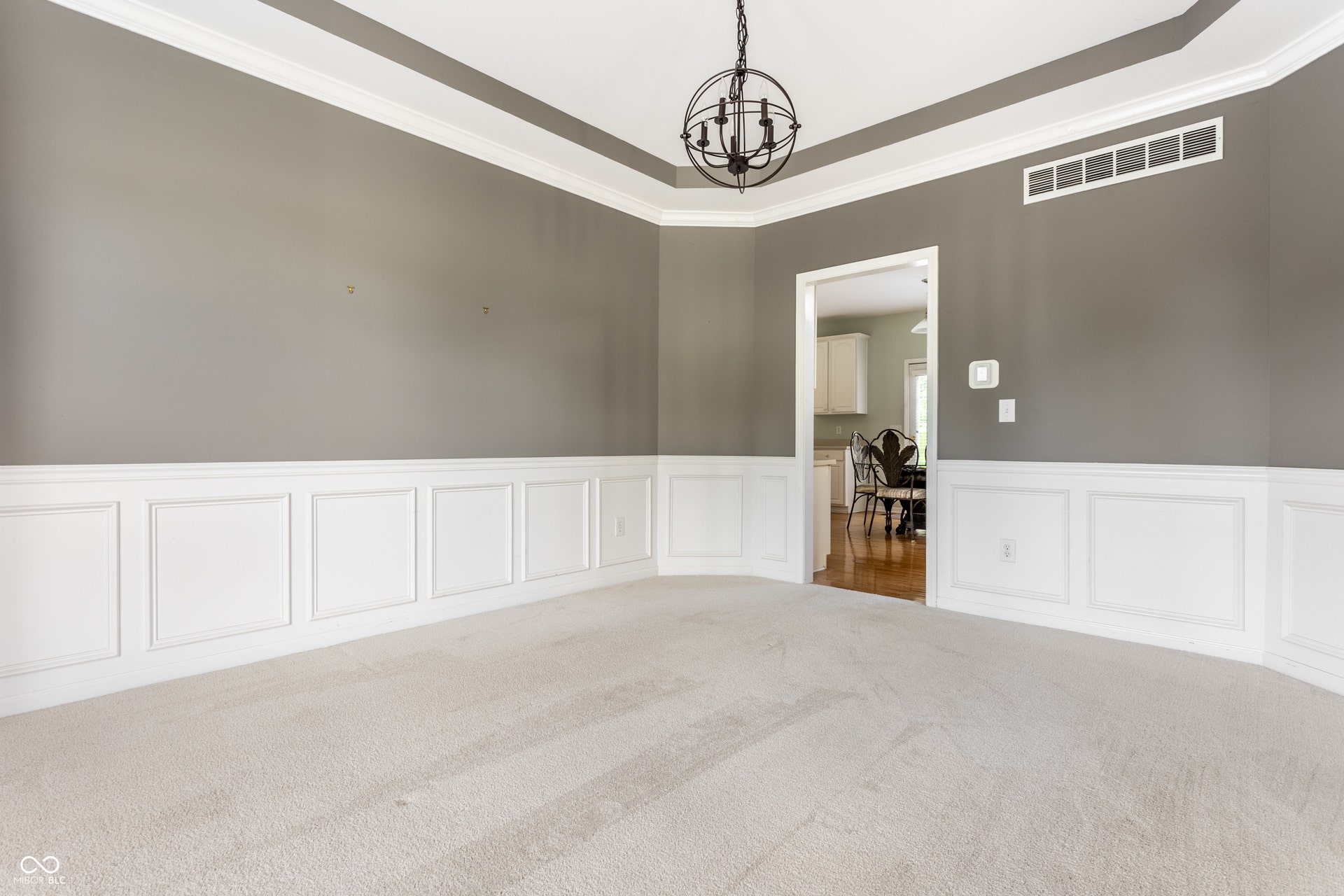 Tray ceiling, crown molding, wall paneling, flush-mount chandelier, and broad entryway