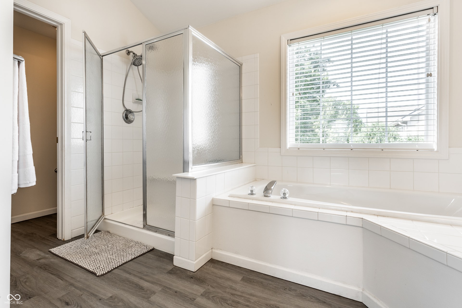 Built-in soaking tub with chrome fixtures, glass-enclosed shower, white tile accents