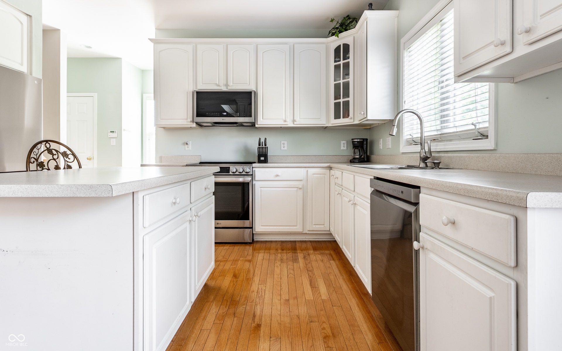 White cabinetry, stainless steel appliances, light-toned countertops, and wood-finish flooring