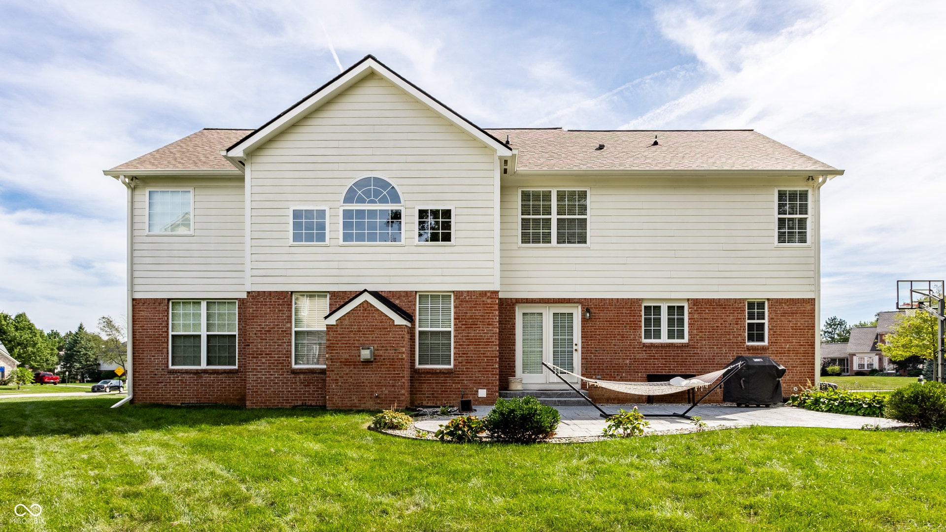Rear exterior with brick and siding facade, patio, and expansive lawn