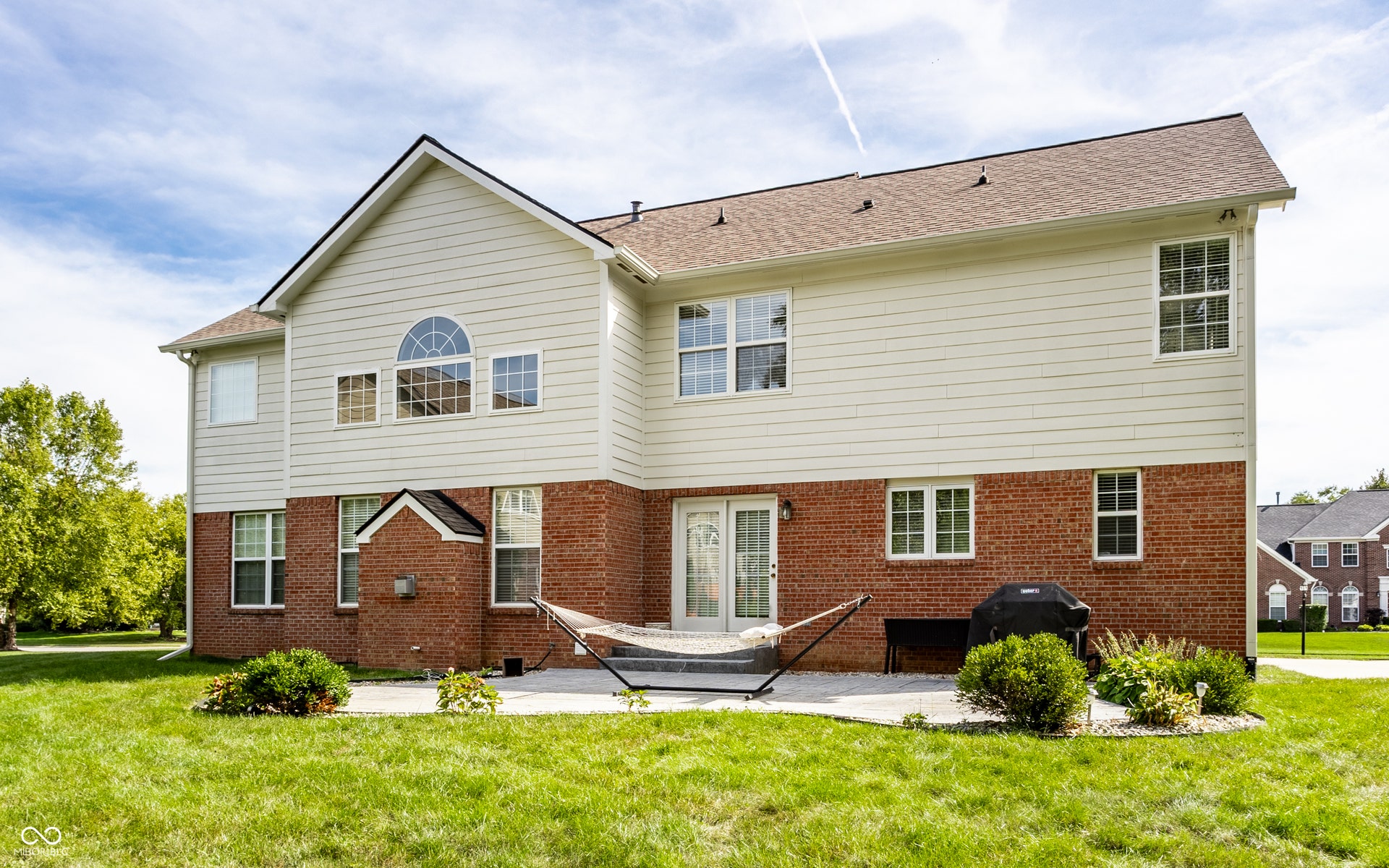 Expansive backyard with a manicured lawn, brick and siding exterior, and a spacious patio