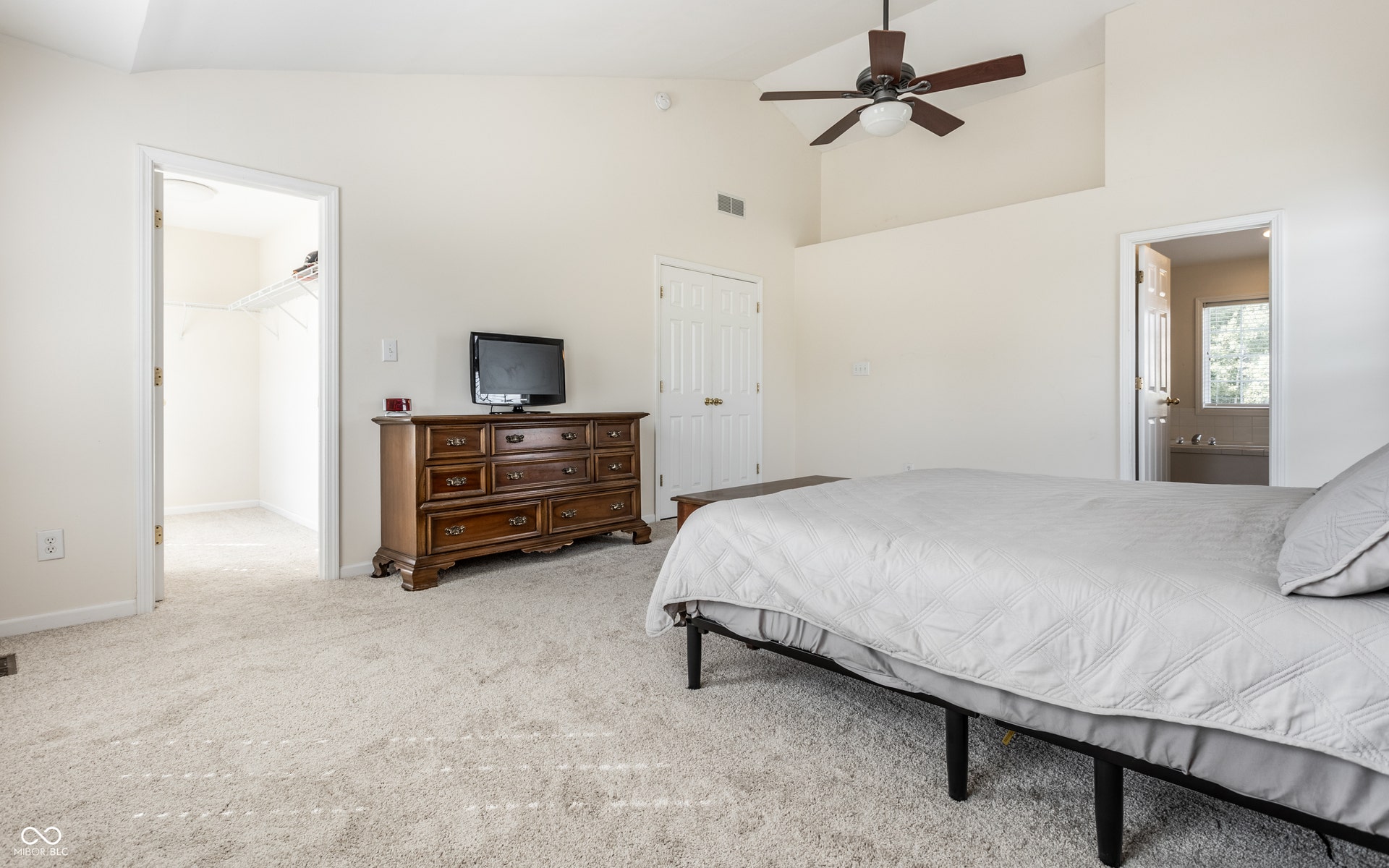 Vaulted ceiling, ceiling fan, plush carpet flooring, walk-in closet, and an attached bathroom