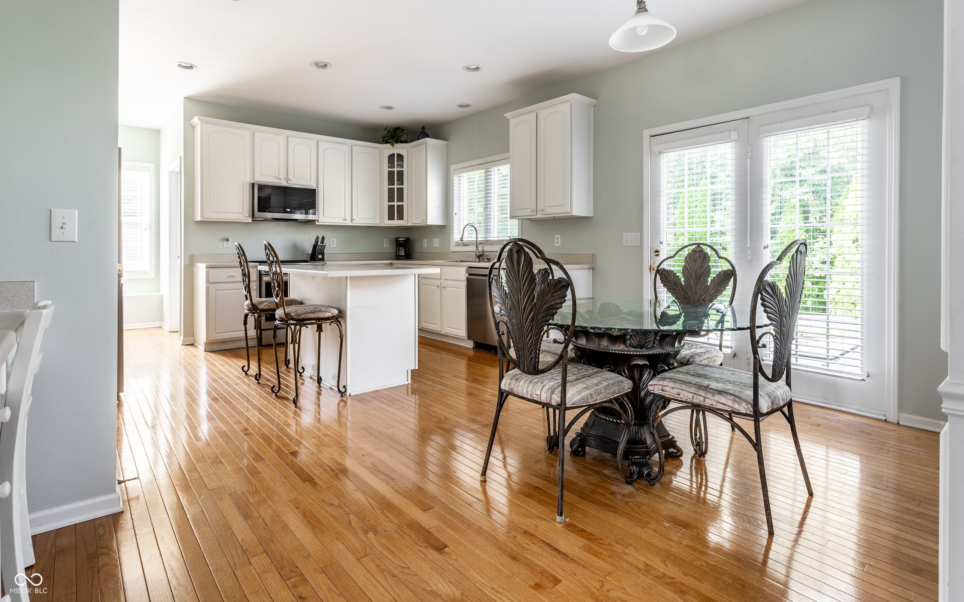 Kitchen featuring hardwood flooring, white cabinetry, stainless steel appliances, a kitchen island and breakfast bar.