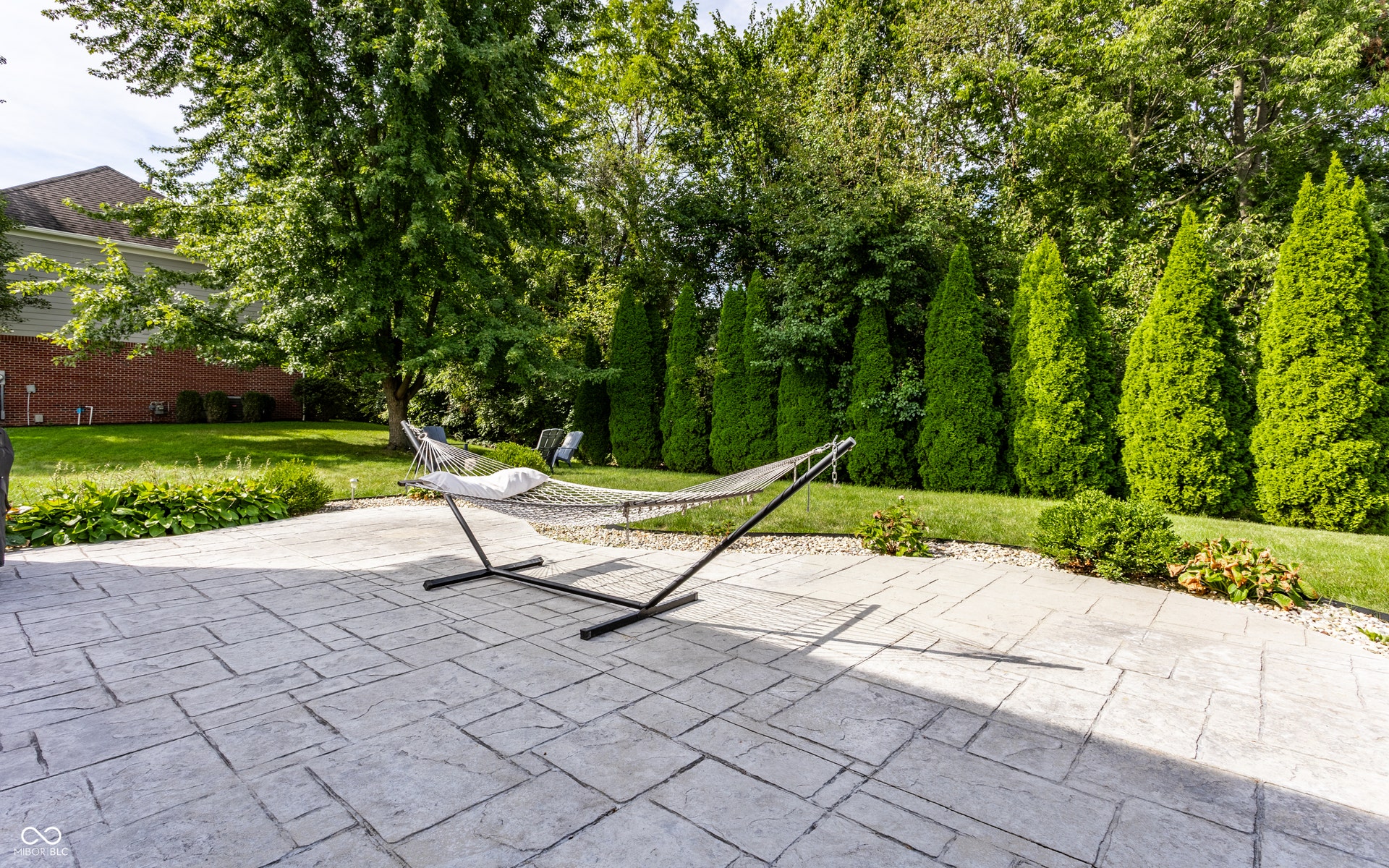 Expansive stamped concrete patio with surrounding green lawn and mature trees