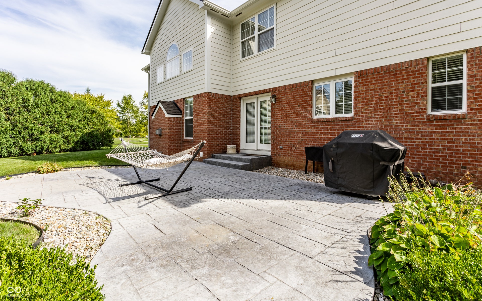 Expansive stamped concrete patio with direct access to interior via French doors, bordered by mature landscaping and a generous lawn area