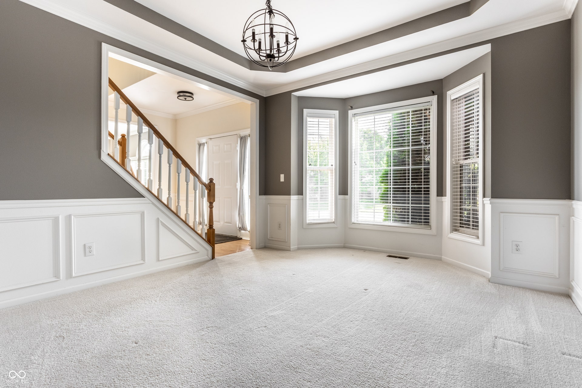 Bay window with multiple panels, tray ceiling, wainscoting, staircase with wood handrail, and an orb chandelier