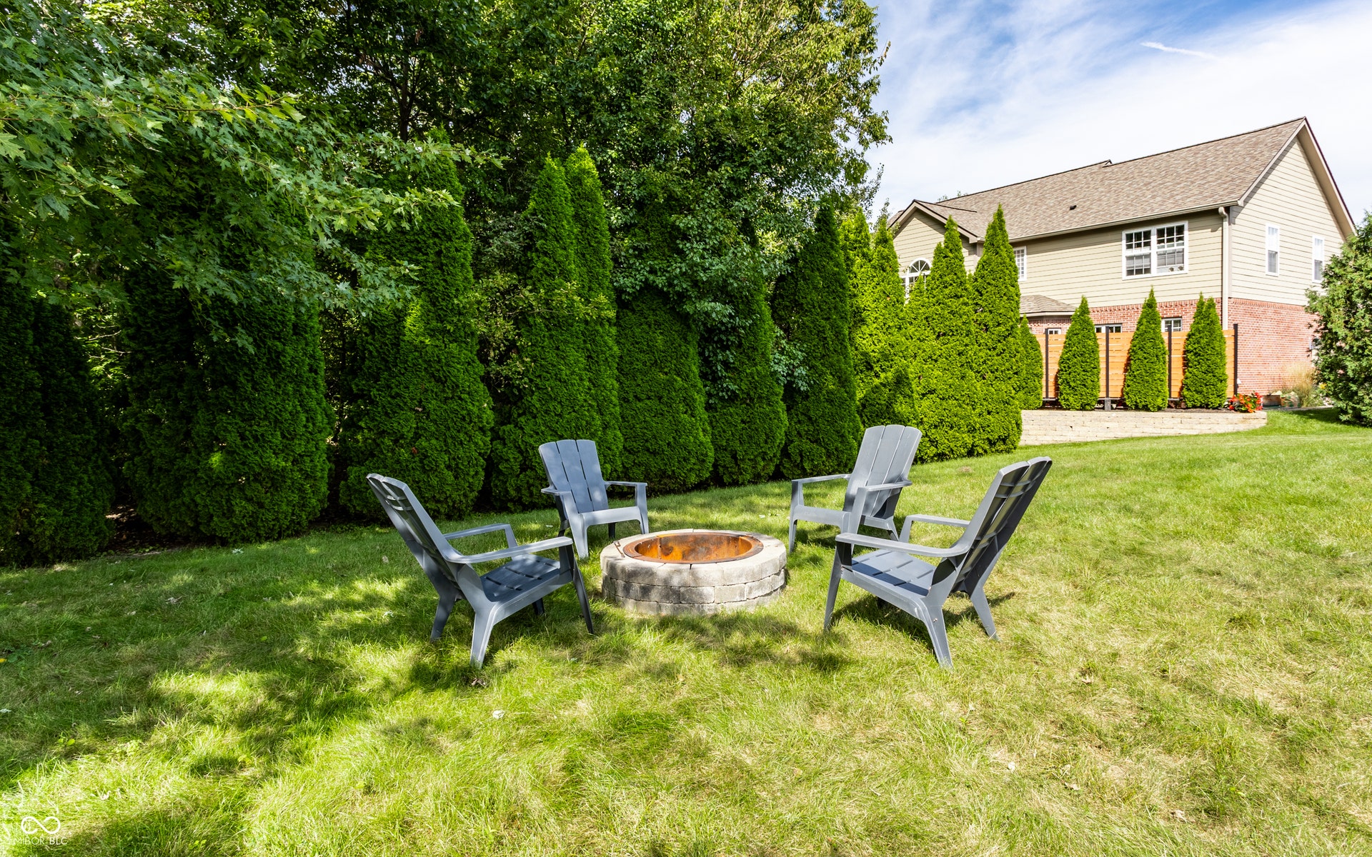Expansive lawn with a stone-finish fire pit, bordered by a privacy hedge and established trees