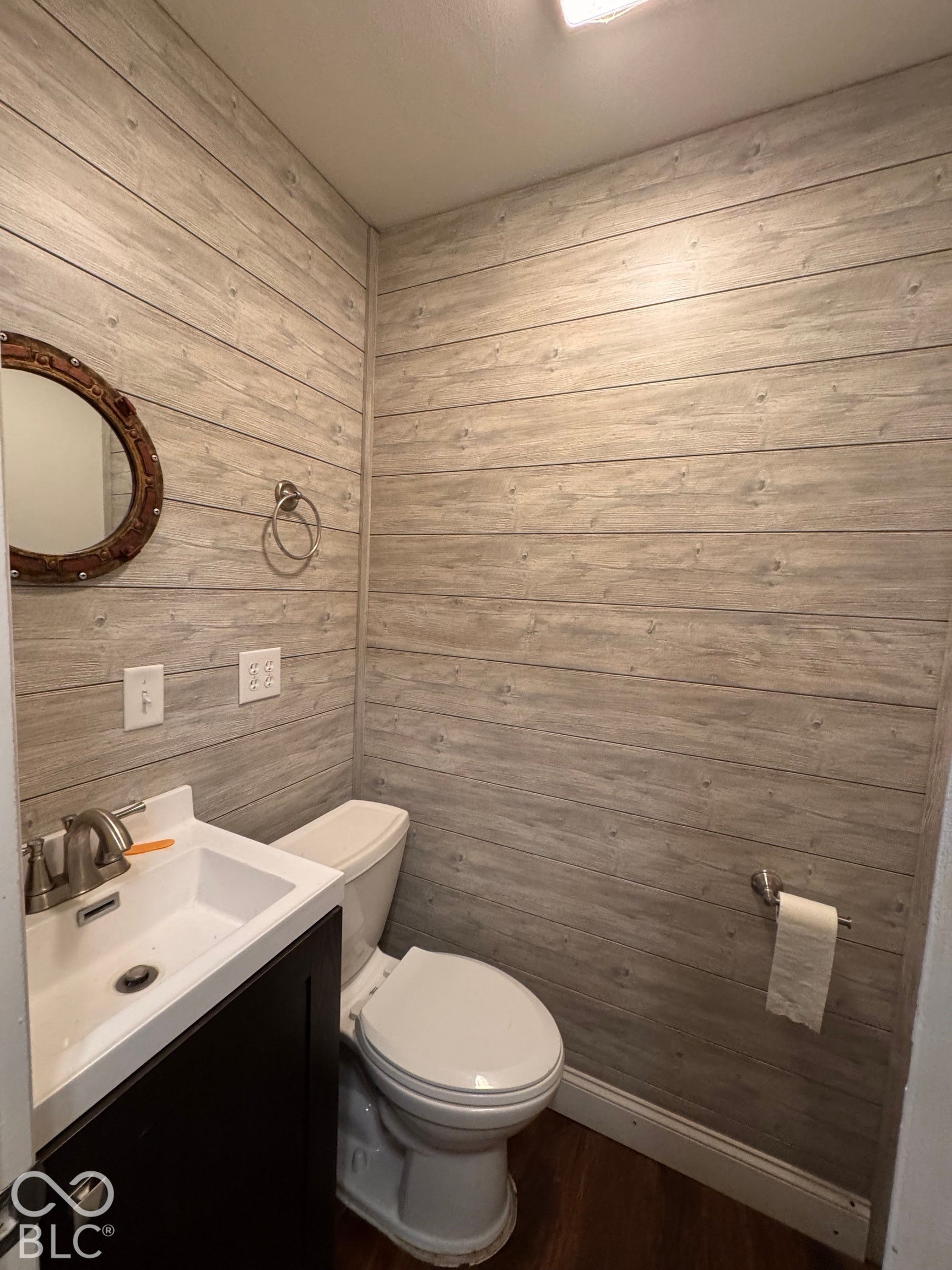 Horizontal wood-finish wall paneling, dark-tone vanity cabinet, rectangular integrated basin, polished metal faucet, and circular wall-mounted mirror