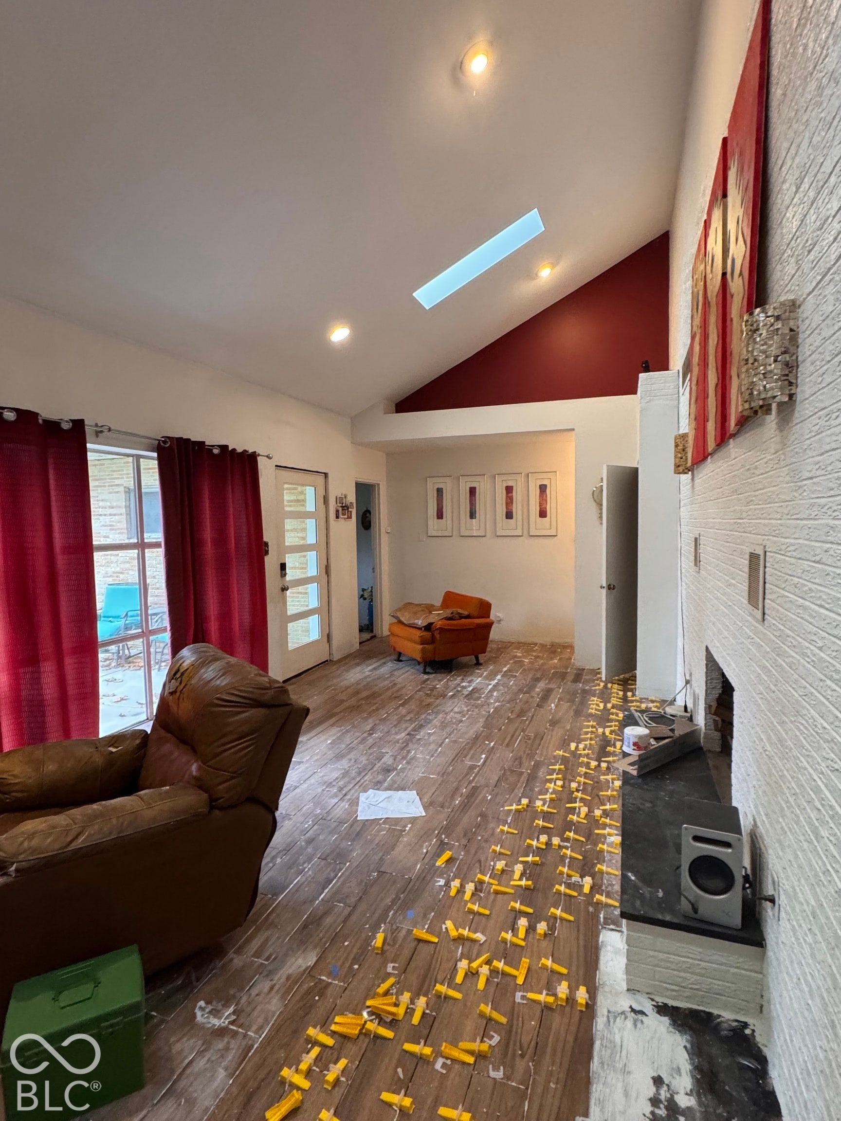 Vaulted ceilings featuring a skylight, wood-finish flooring, and a floor-to-ceiling painted brick wall with an integrated fireplace hearth