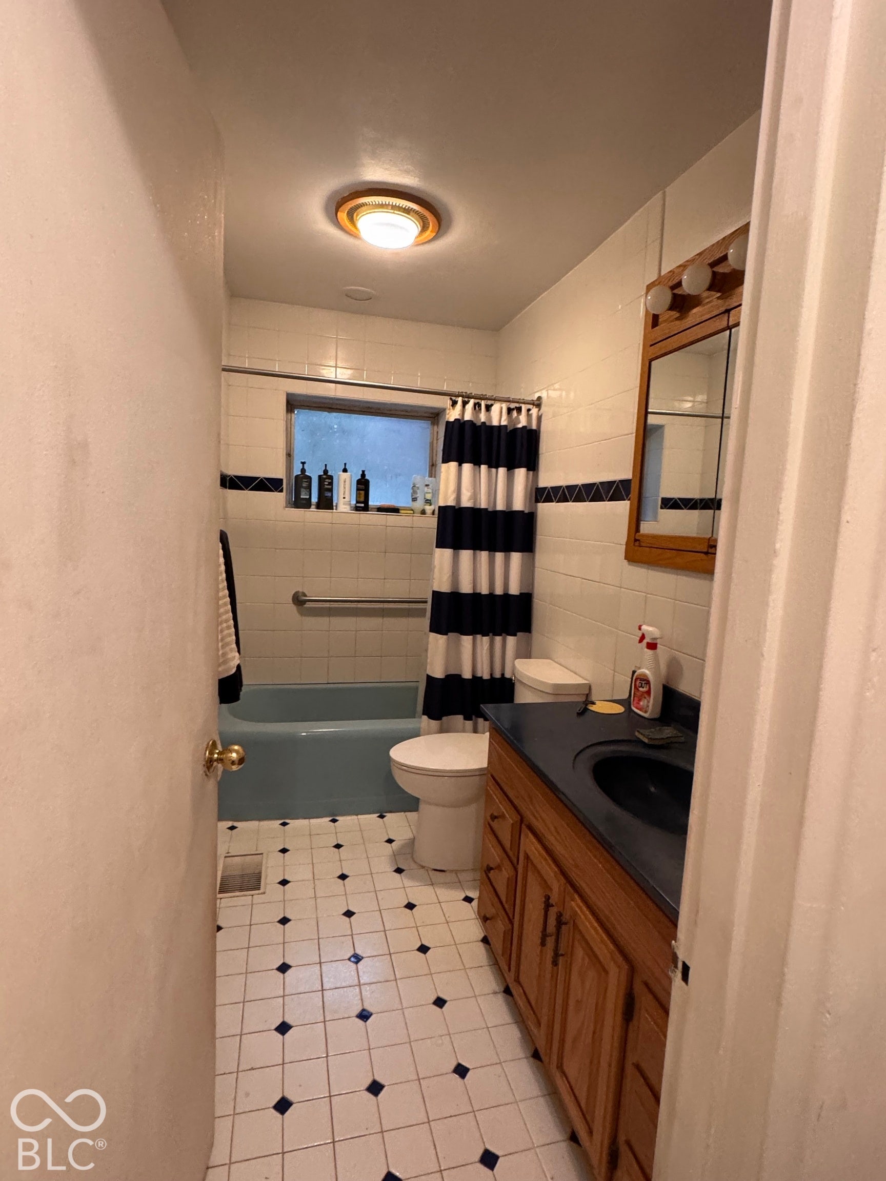 Bathroom featuring a vanity with dark countertop, built-in wooden cabinetry, wall-mounted mirror, tiled shower walls with decorative inlay, and a tub