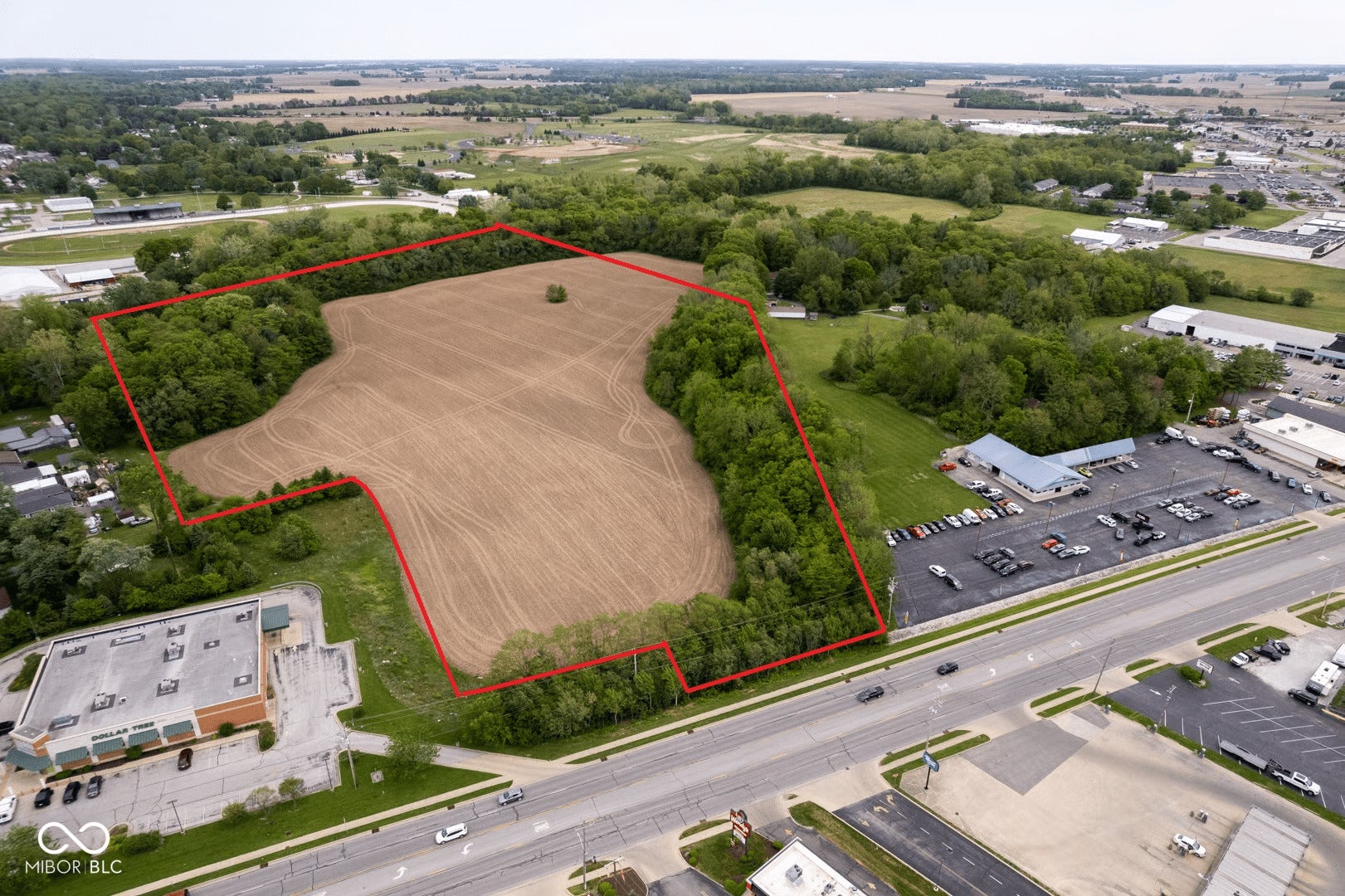 Approximately 40+ acres of cleared agricultural land with mature tree lines defining the perimeter, positioned along a major commercial corridor with immediate highway access