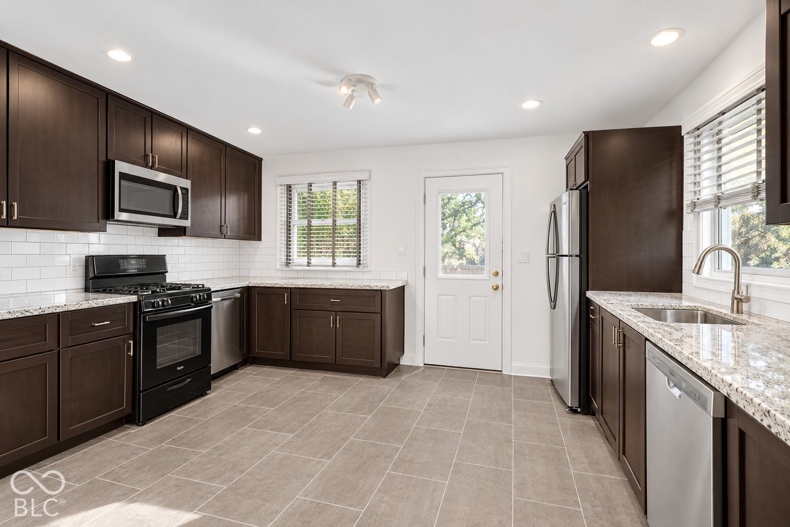 Kitchen featuring dark wood cabinetry, light granite countertops, stainless steel appliances, a subway tile backsplash, and ceramic tile flooring